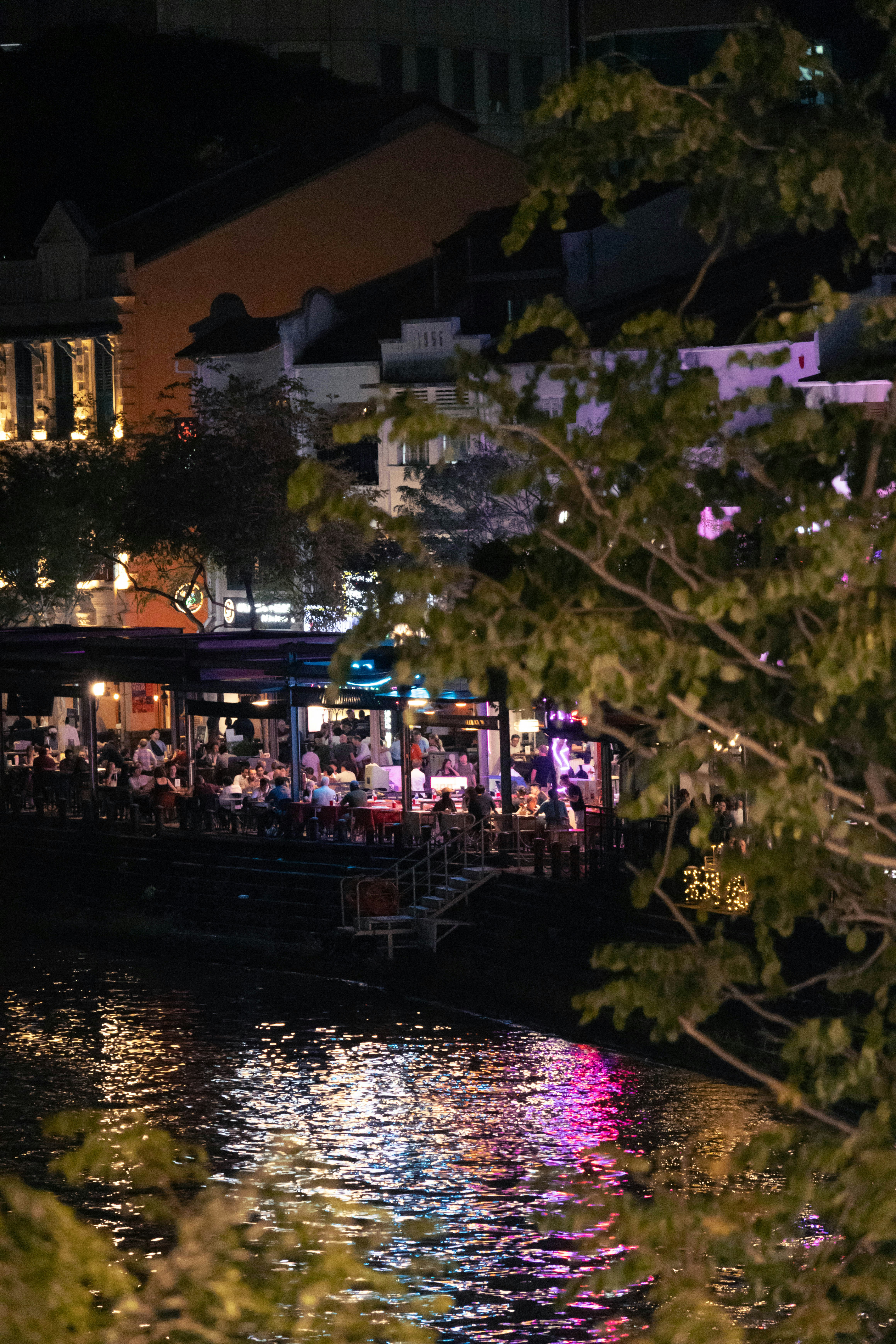 Boats and buildings illuminated at night by the river.