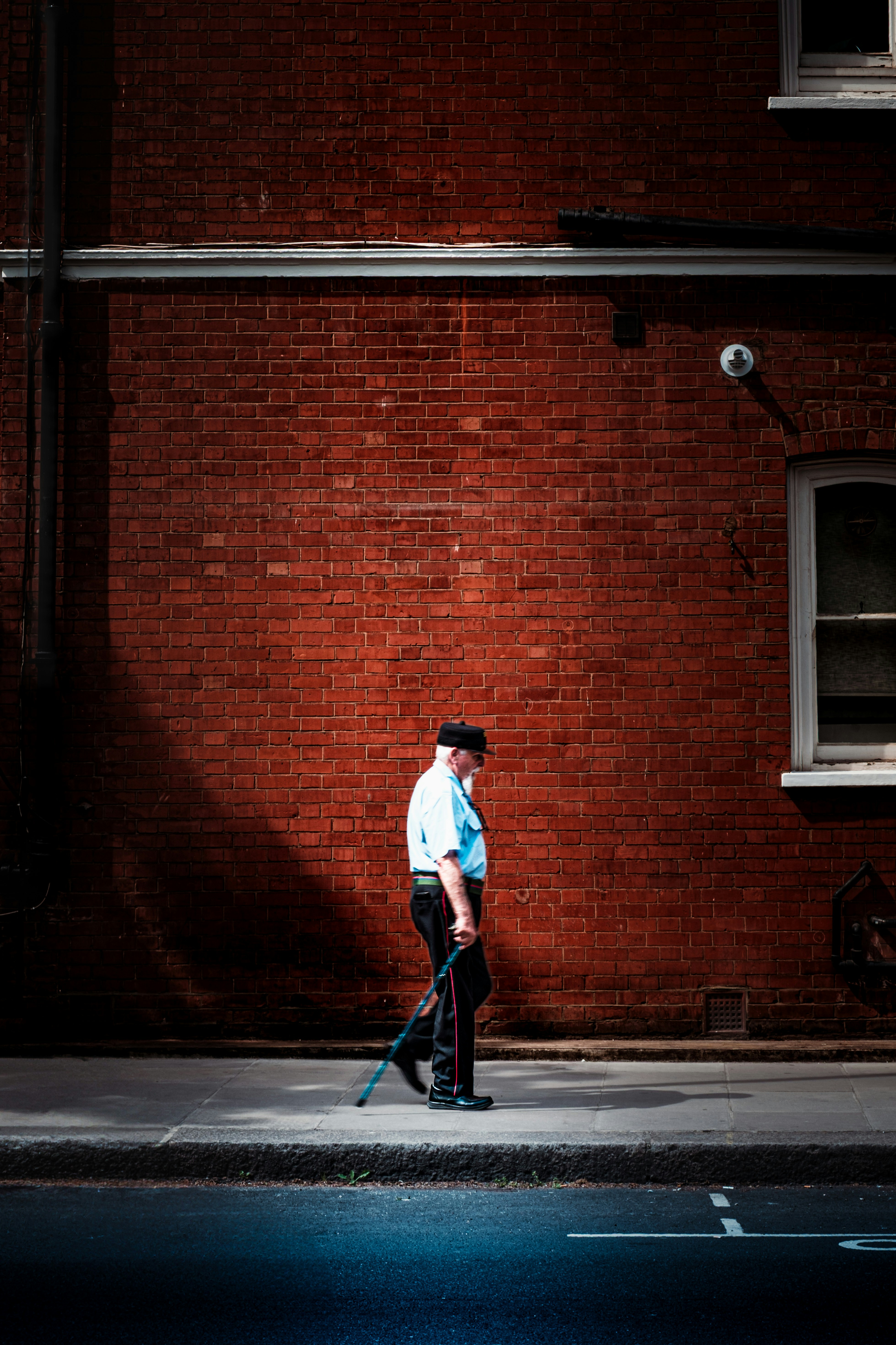 Man with cane walks past brick building