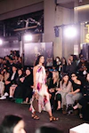 Model walks runway in floral dress with audience watching