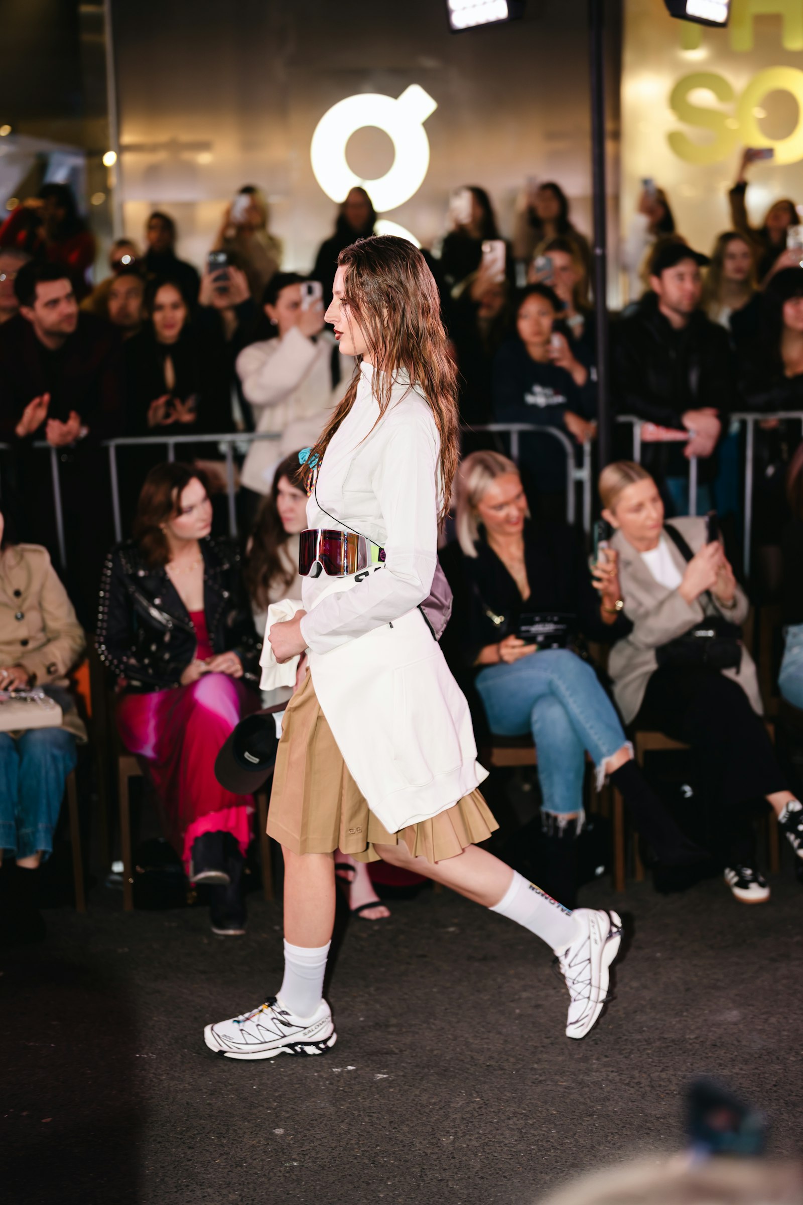 A model walks a lit runway before a seated audience, fashion week 2026