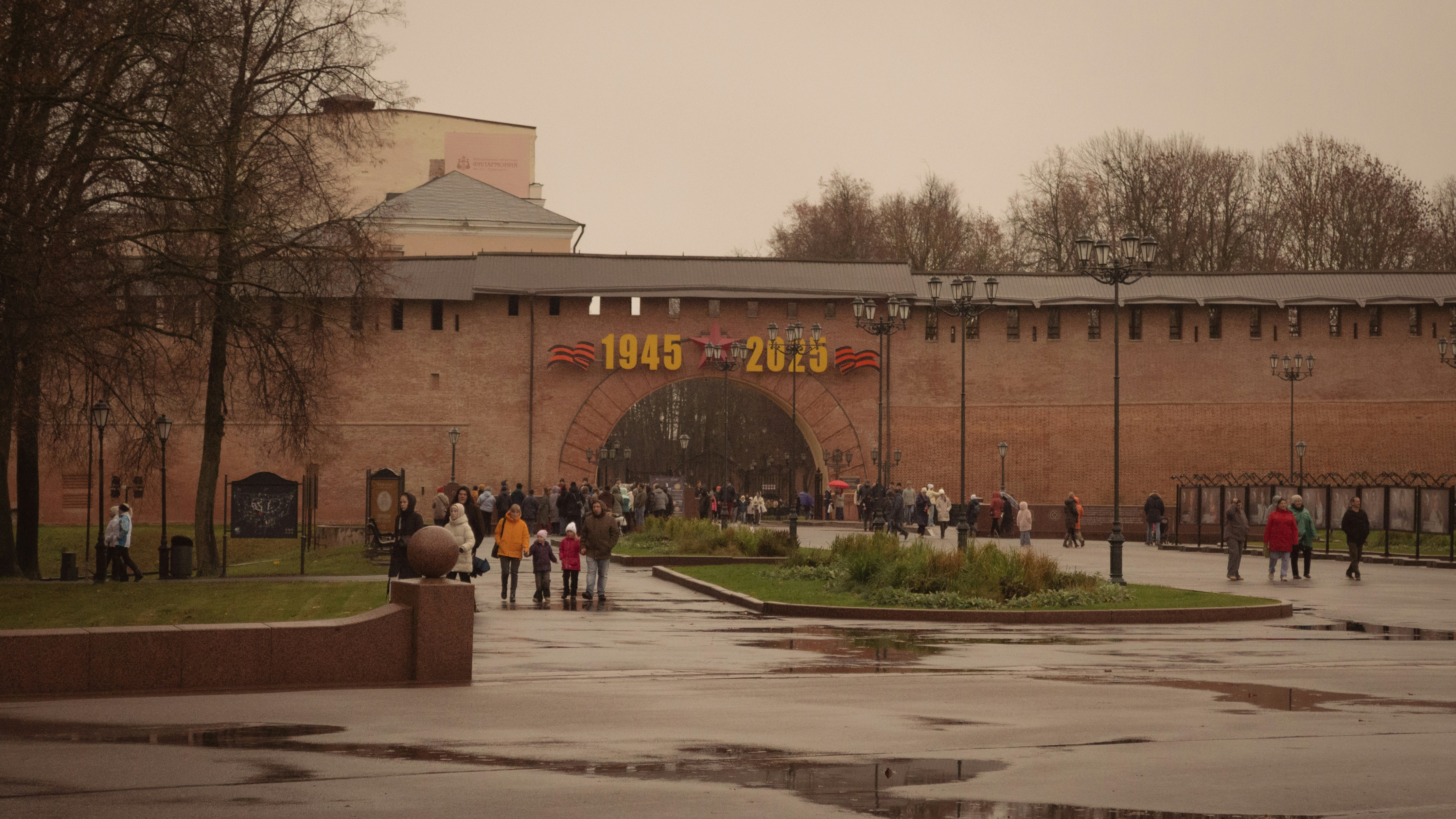 People walk near a brick wall with "1945-2020" sign.