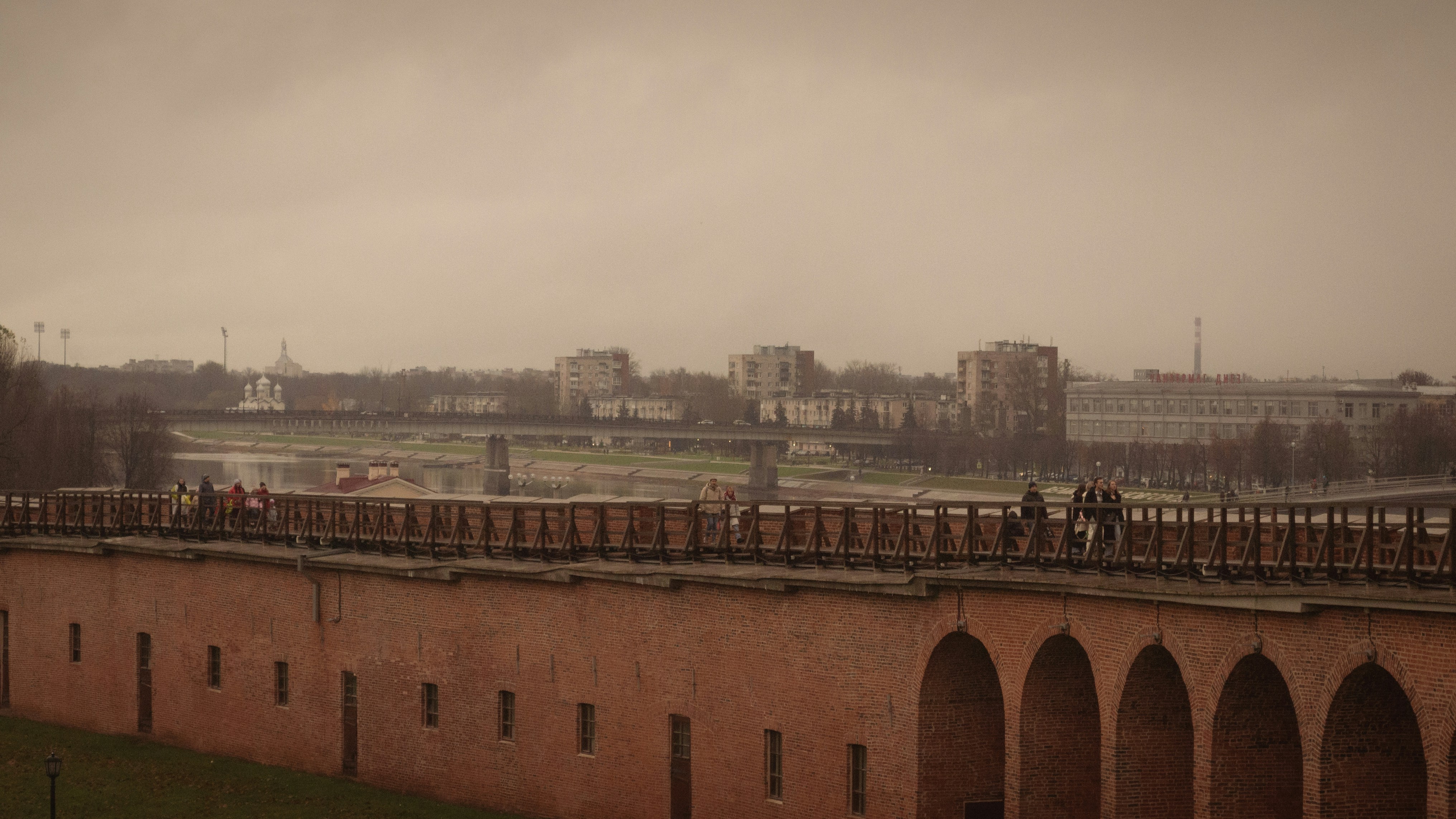 People walk along a brick wall overlooking a city.