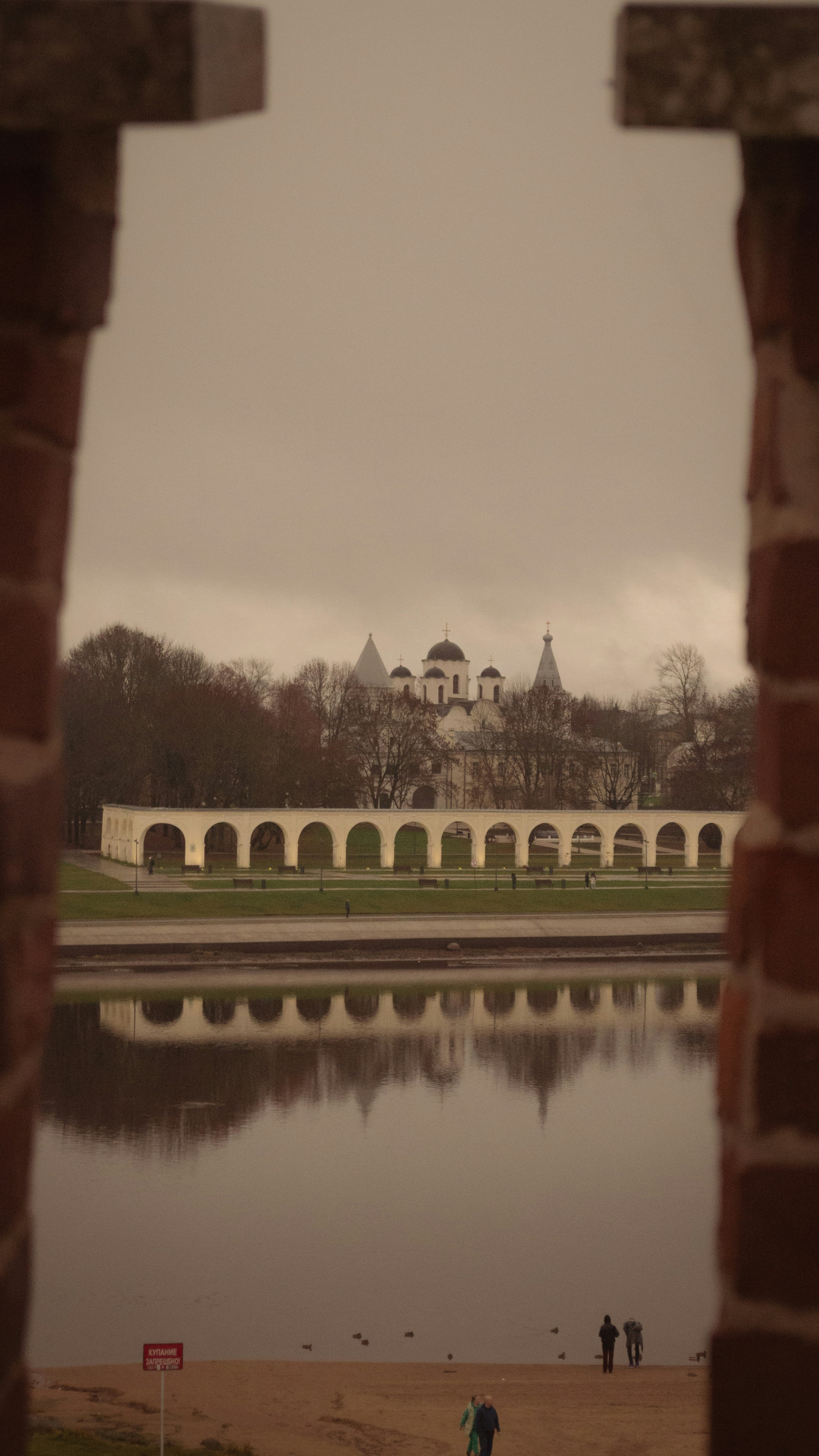 Historic buildings reflected in calm water under cloudy sky.