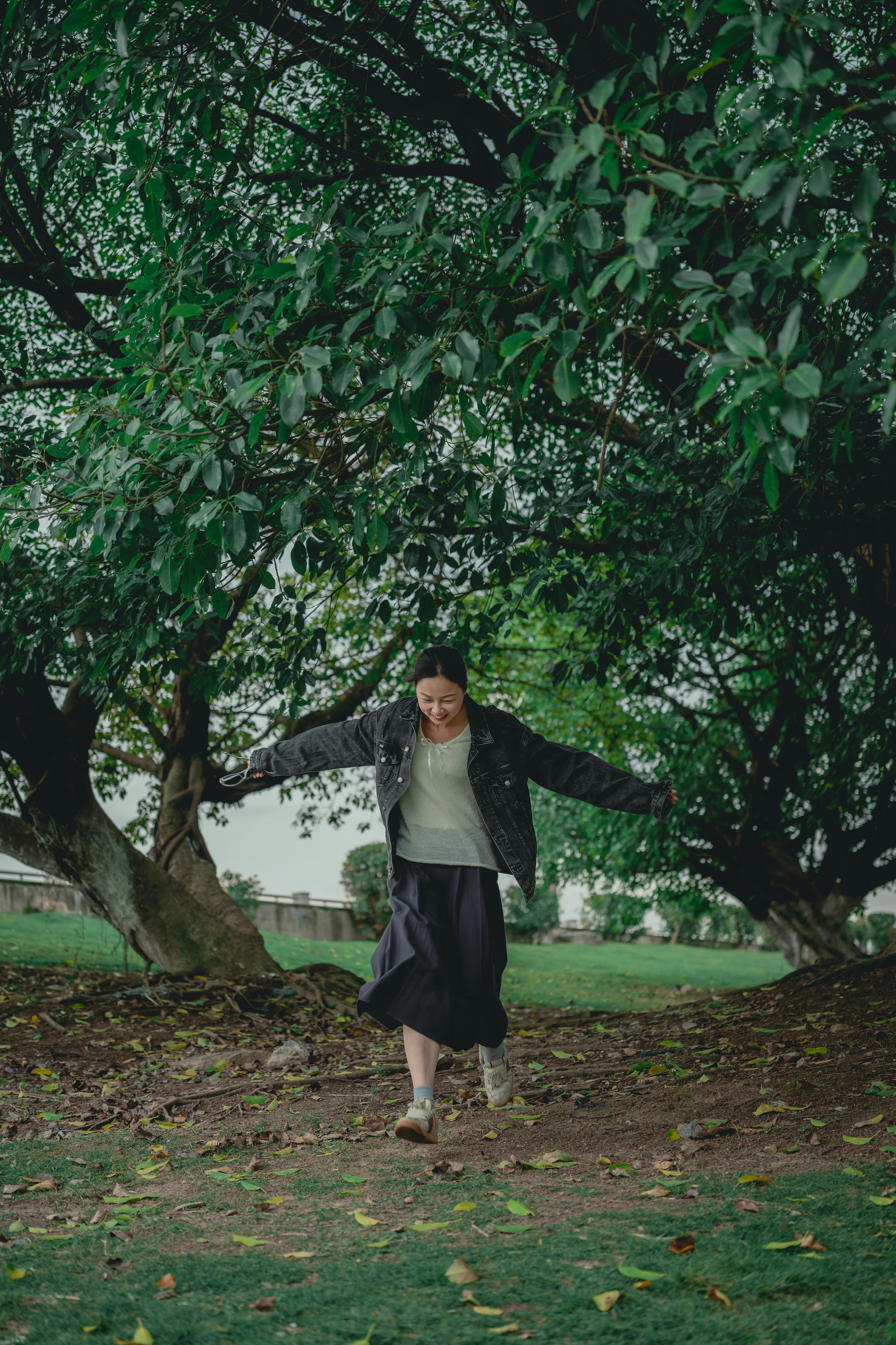 Woman walking with arms outstretched under trees