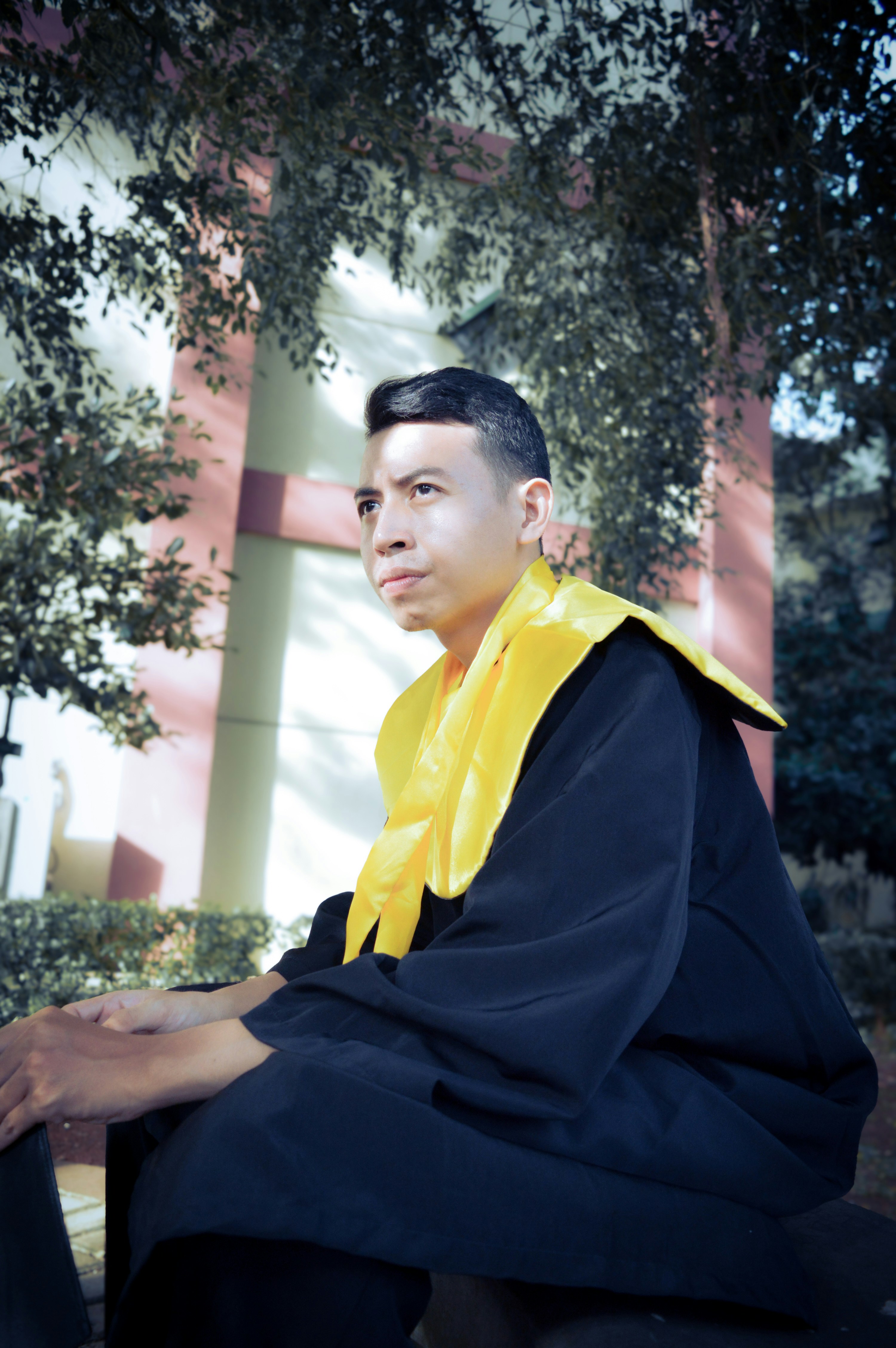 A man in graduation gown sitting outdoors
