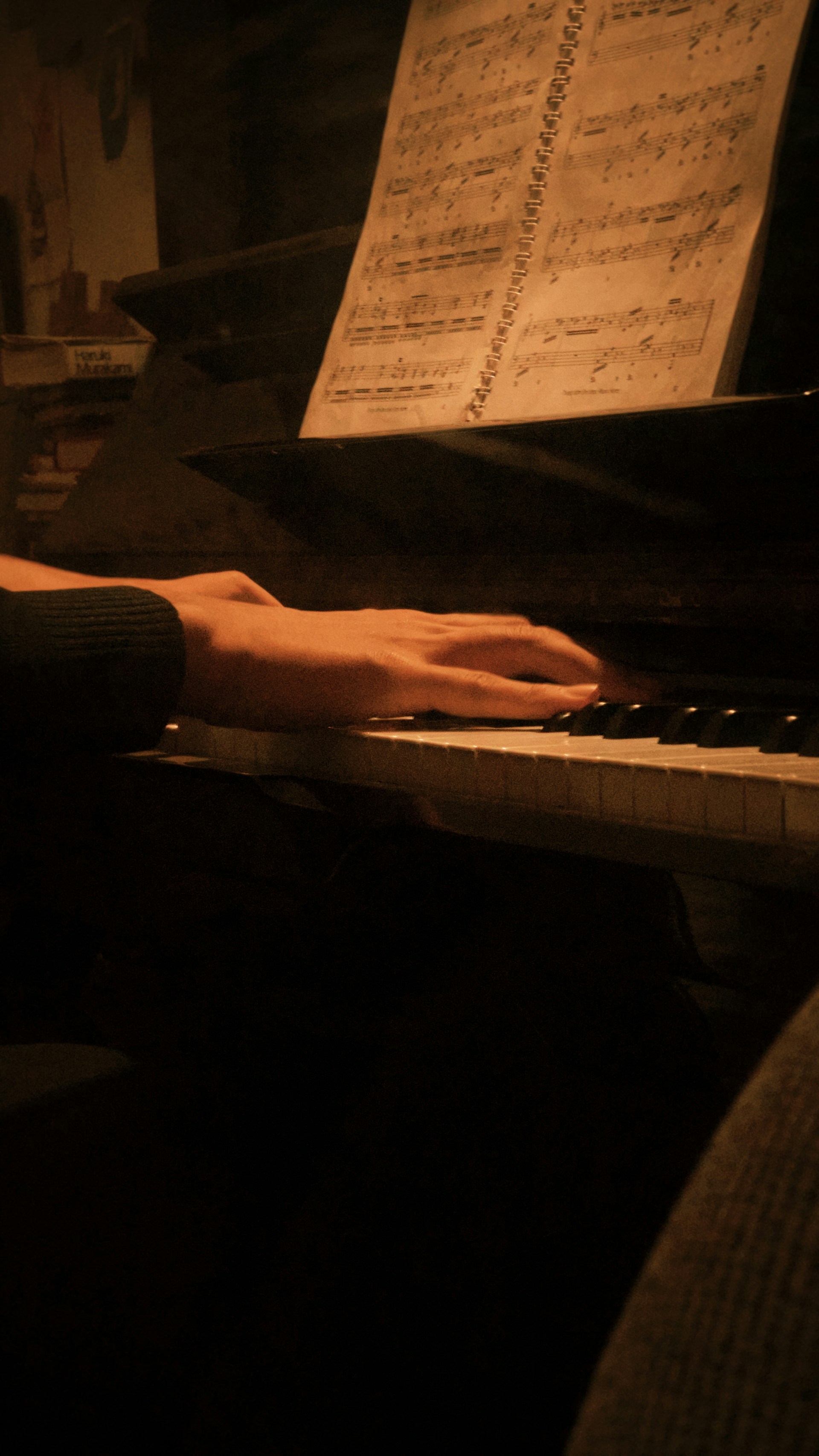 Hands playing a piano with sheet music.