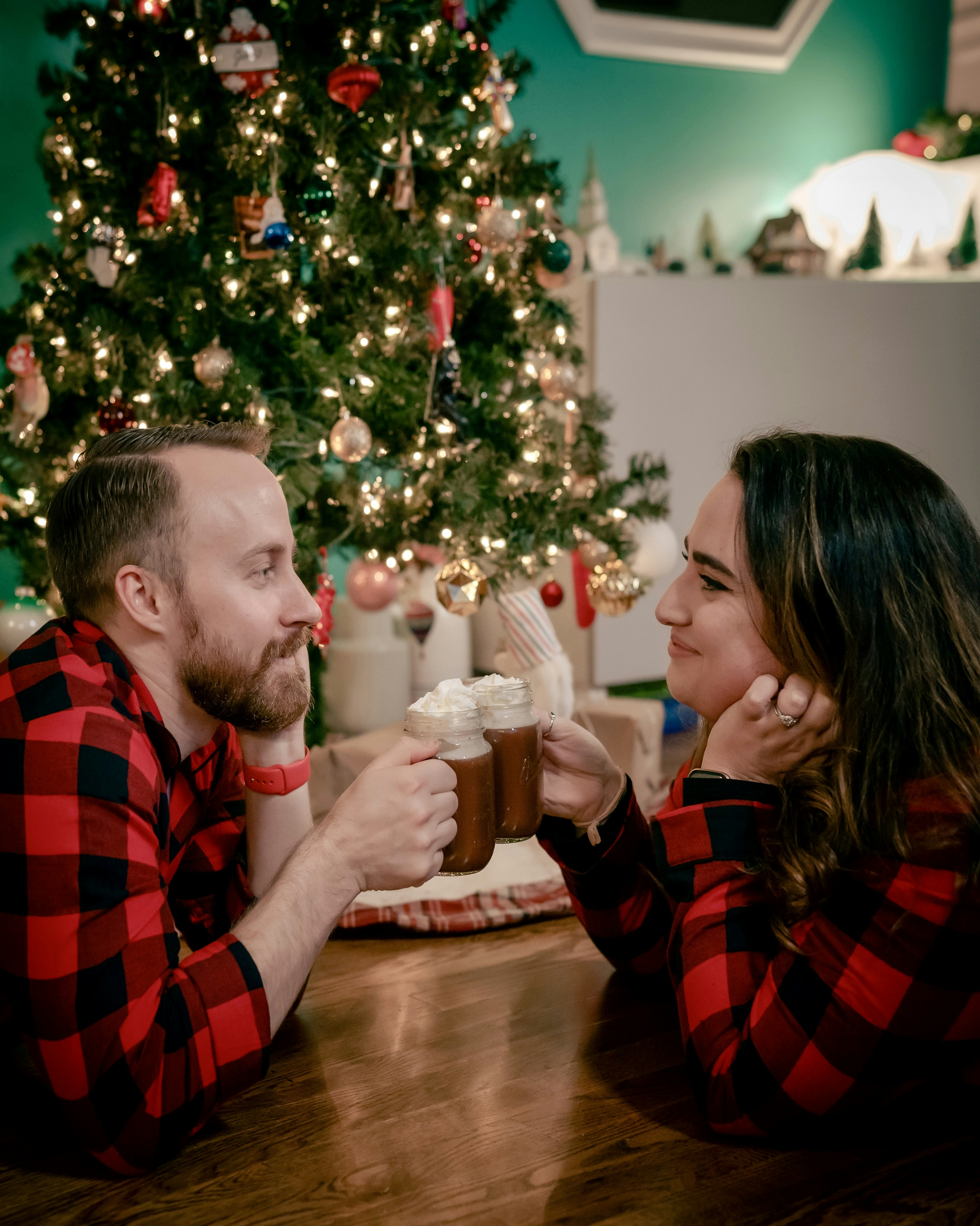 Pareja en pijama a juego compartiendo chocolate caliente junto al árbol de navidad