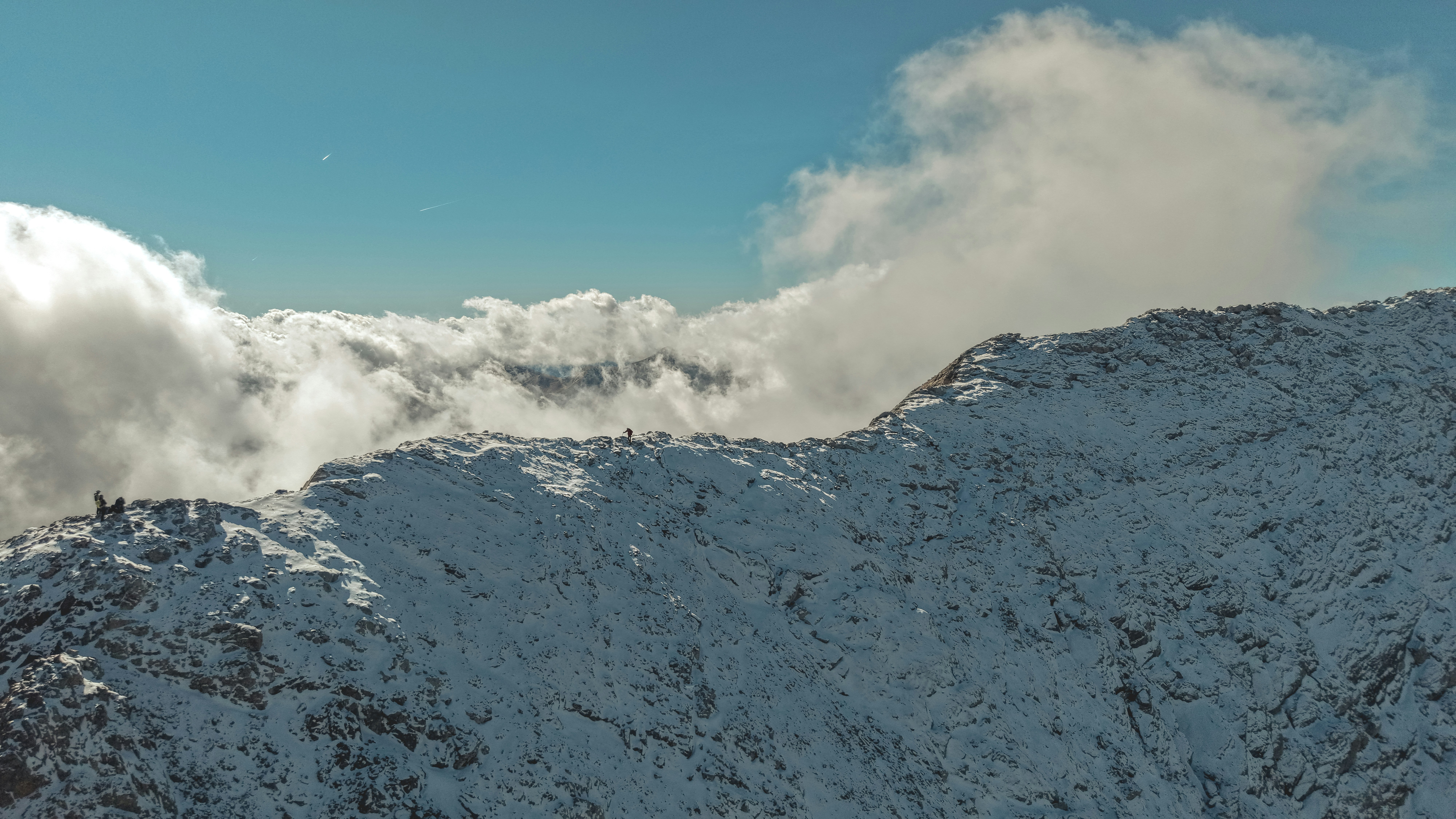 Cime montuose innevate con nuvole ed escursionisti