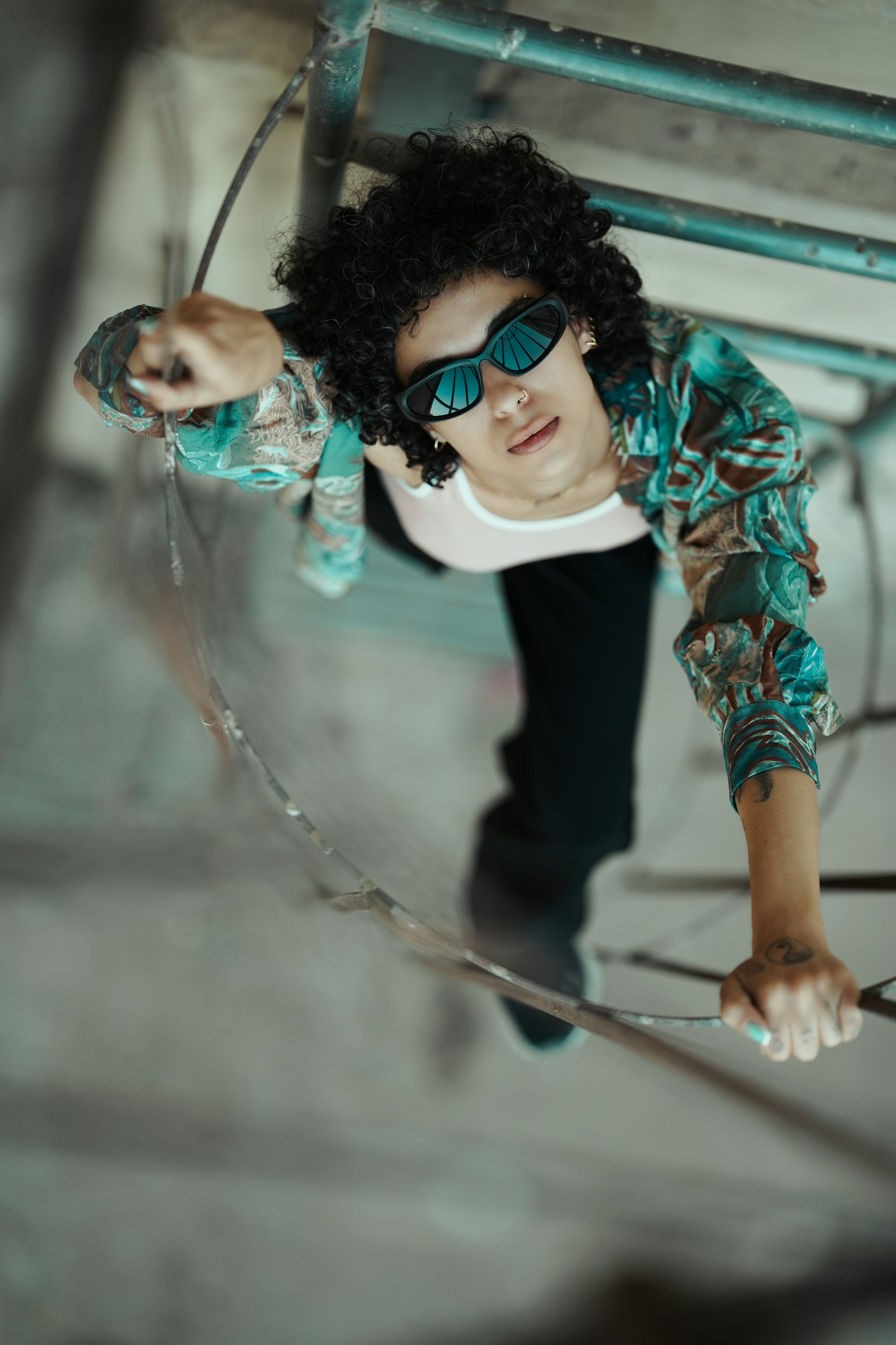 Man with curly hair climbing a metal ladder outdoors.