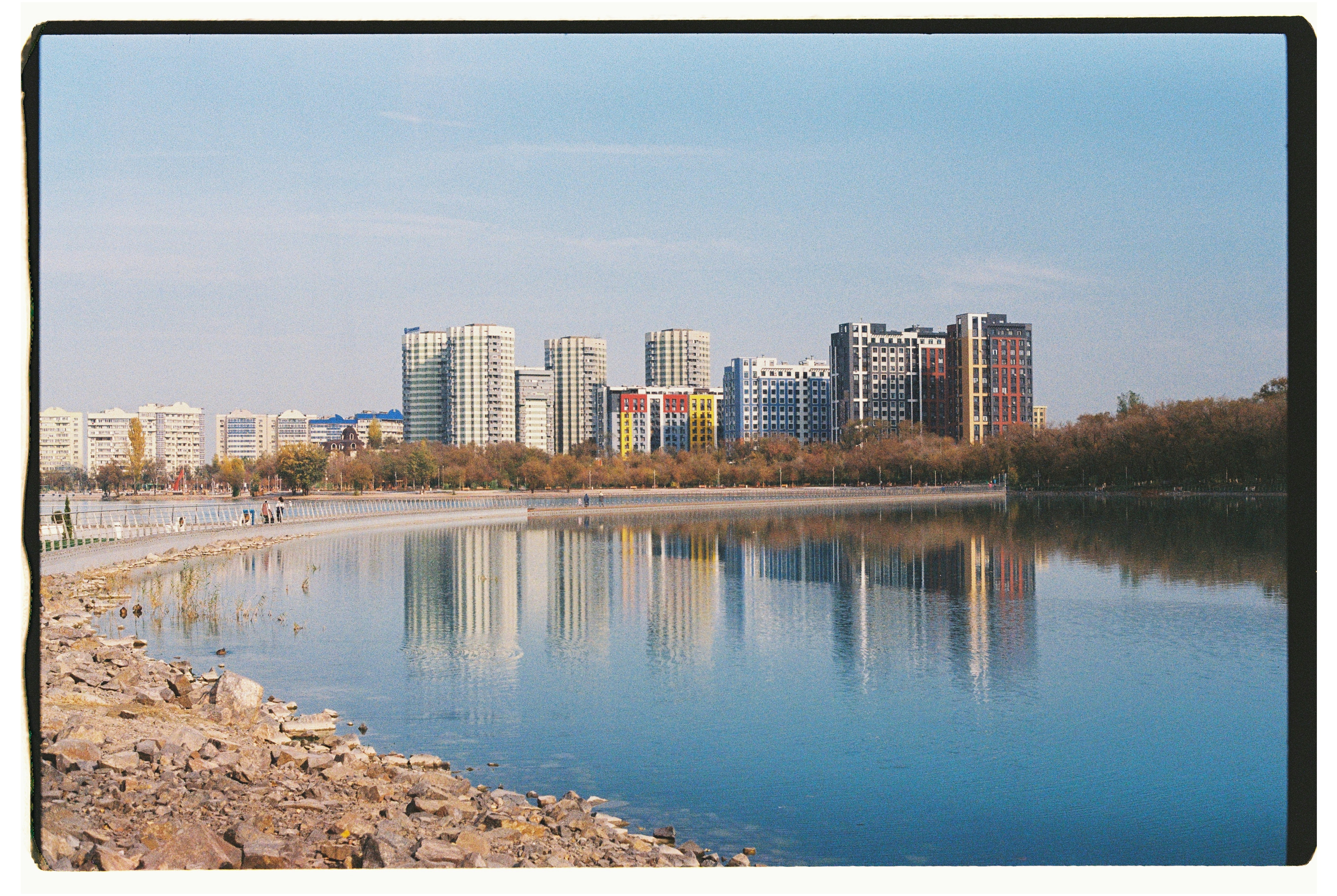 Modern buildings reflected in a calm lake during autumn.