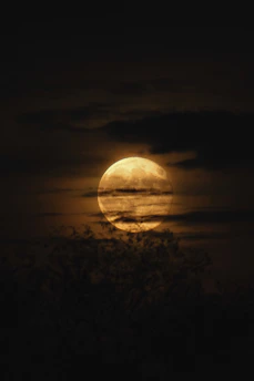 Full moon glowing behind dark clouds at night