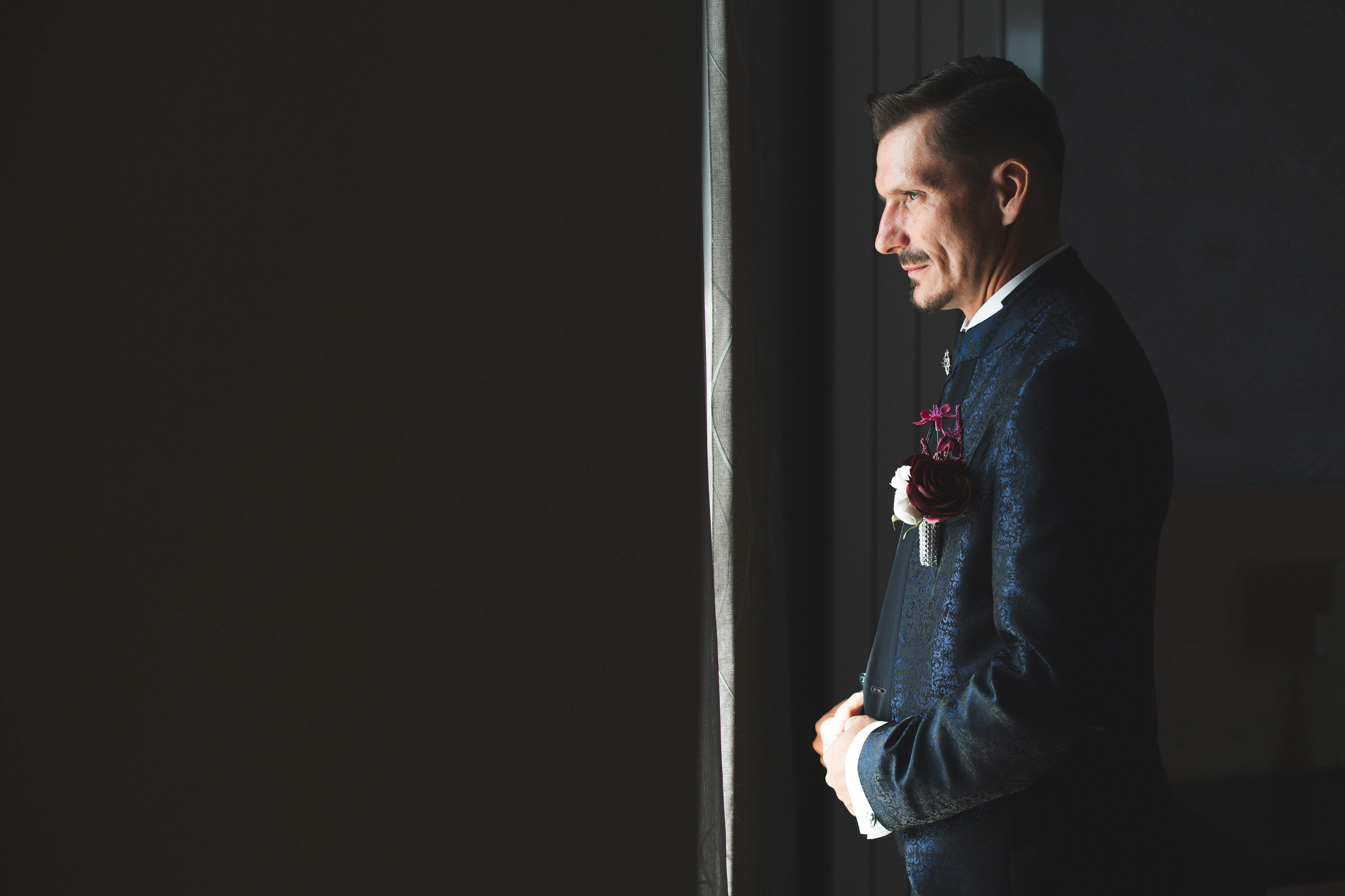 Groom in a room, looking out the window.