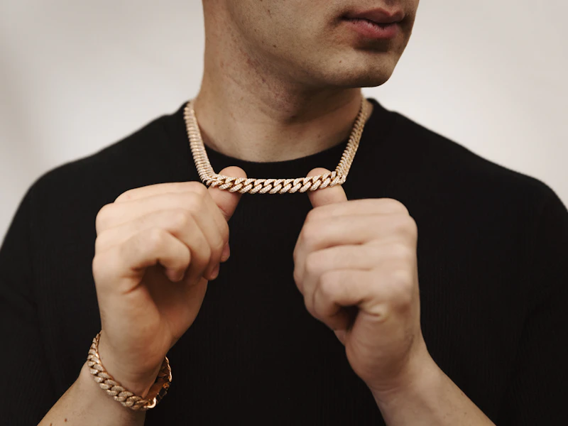 Adult man adjusting a pavé diamond Cuban link chain worn with a matching bracelet over a black shirt