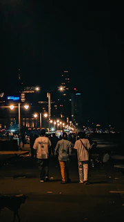 Three people walk along a street at night.