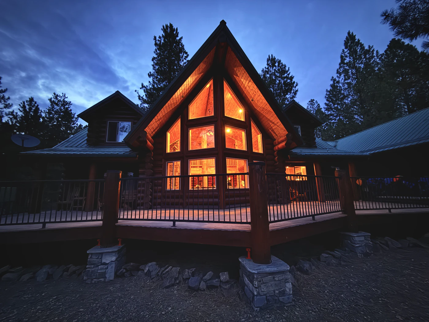 Log home at dusk with glowing prow-front windows and wide deck