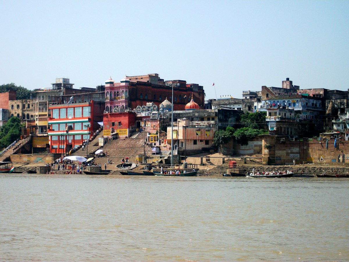 Riverside guesthouses and old buildings lining a Varanasi ghat, seen from a boat on the Ganges