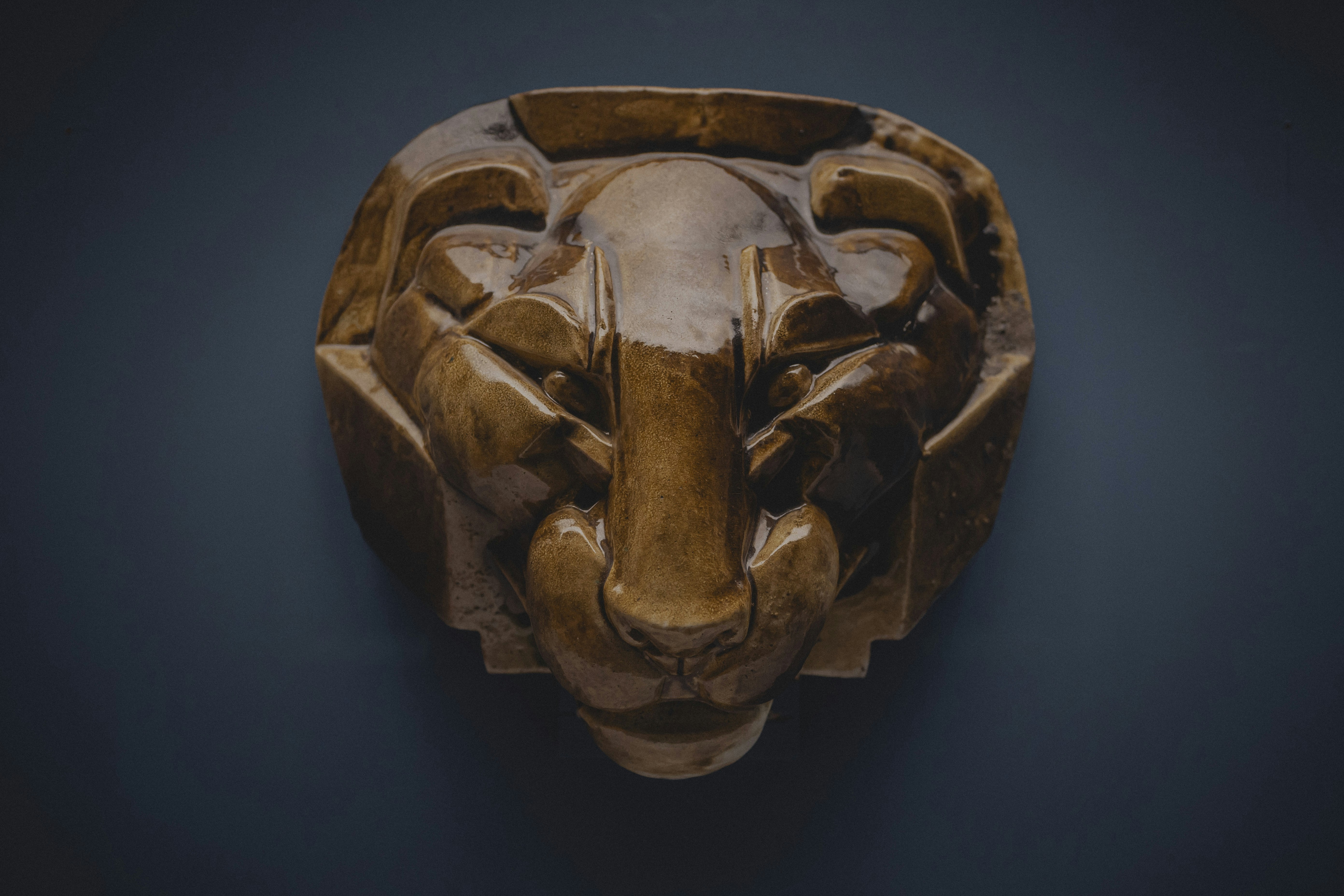 Ein geschnitzter hölzerner Löwenkopf vor dunklem Hintergrund.