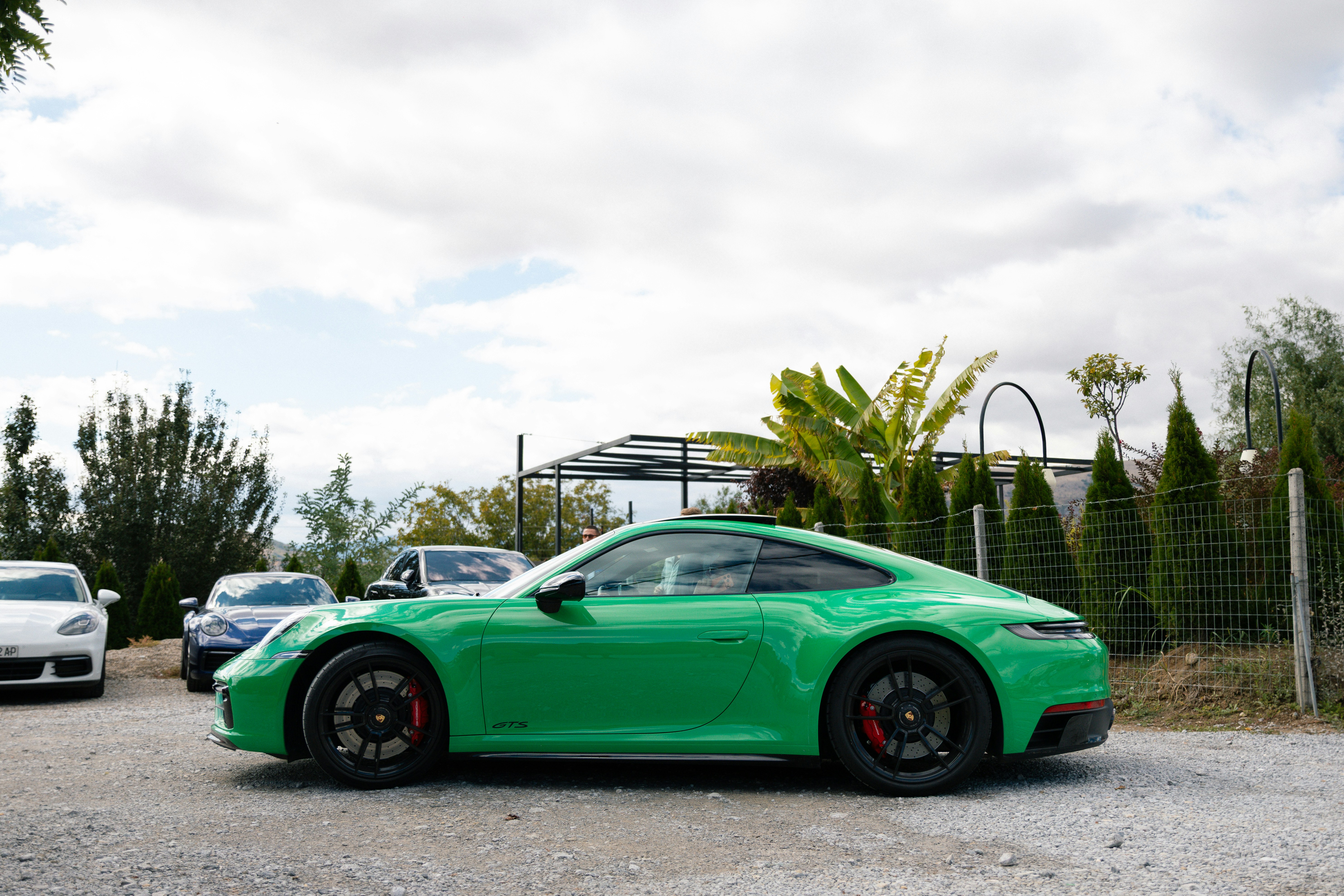 Green porsche sports car parked outdoors with other cars.