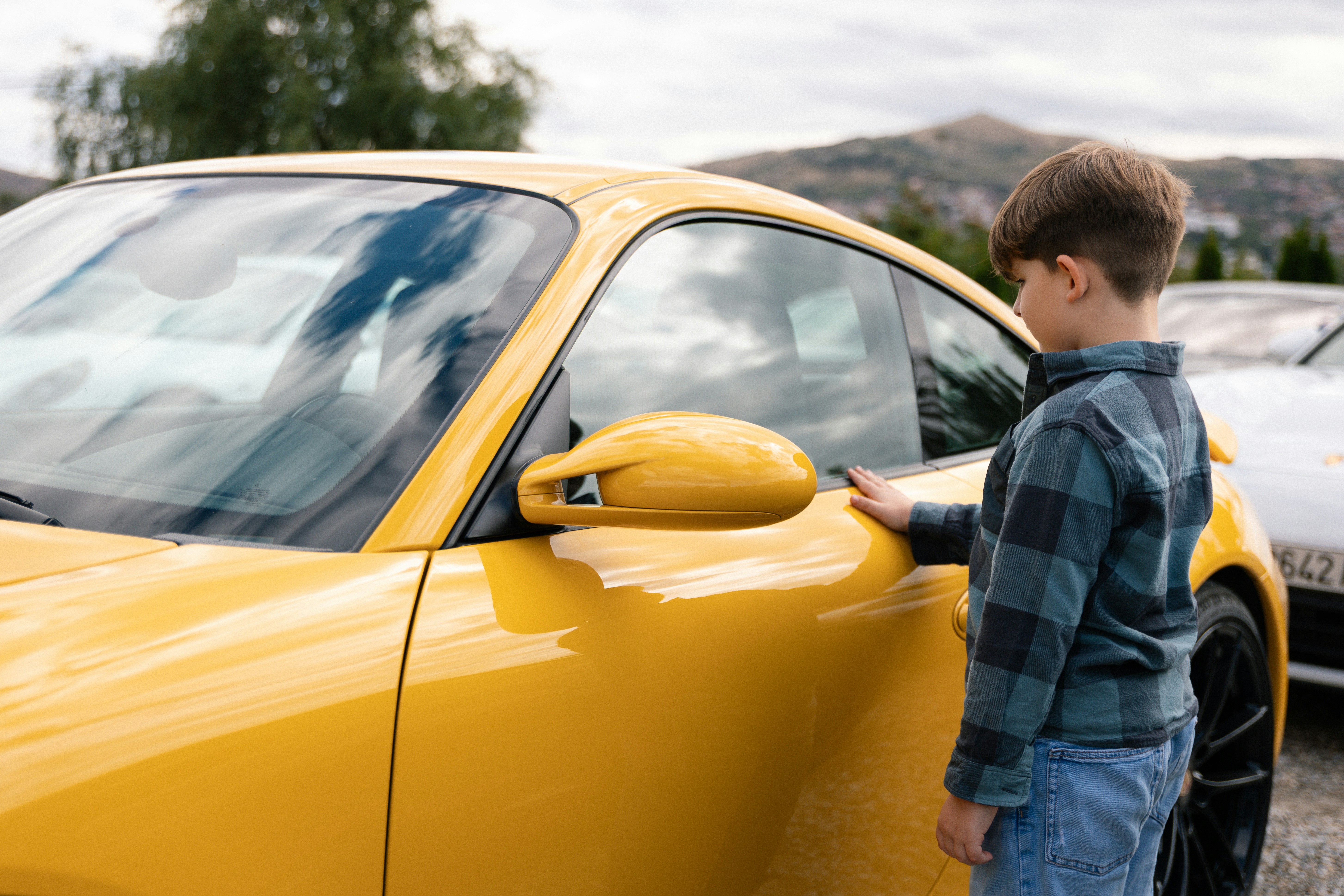 A young boy touches a yellow sports car.