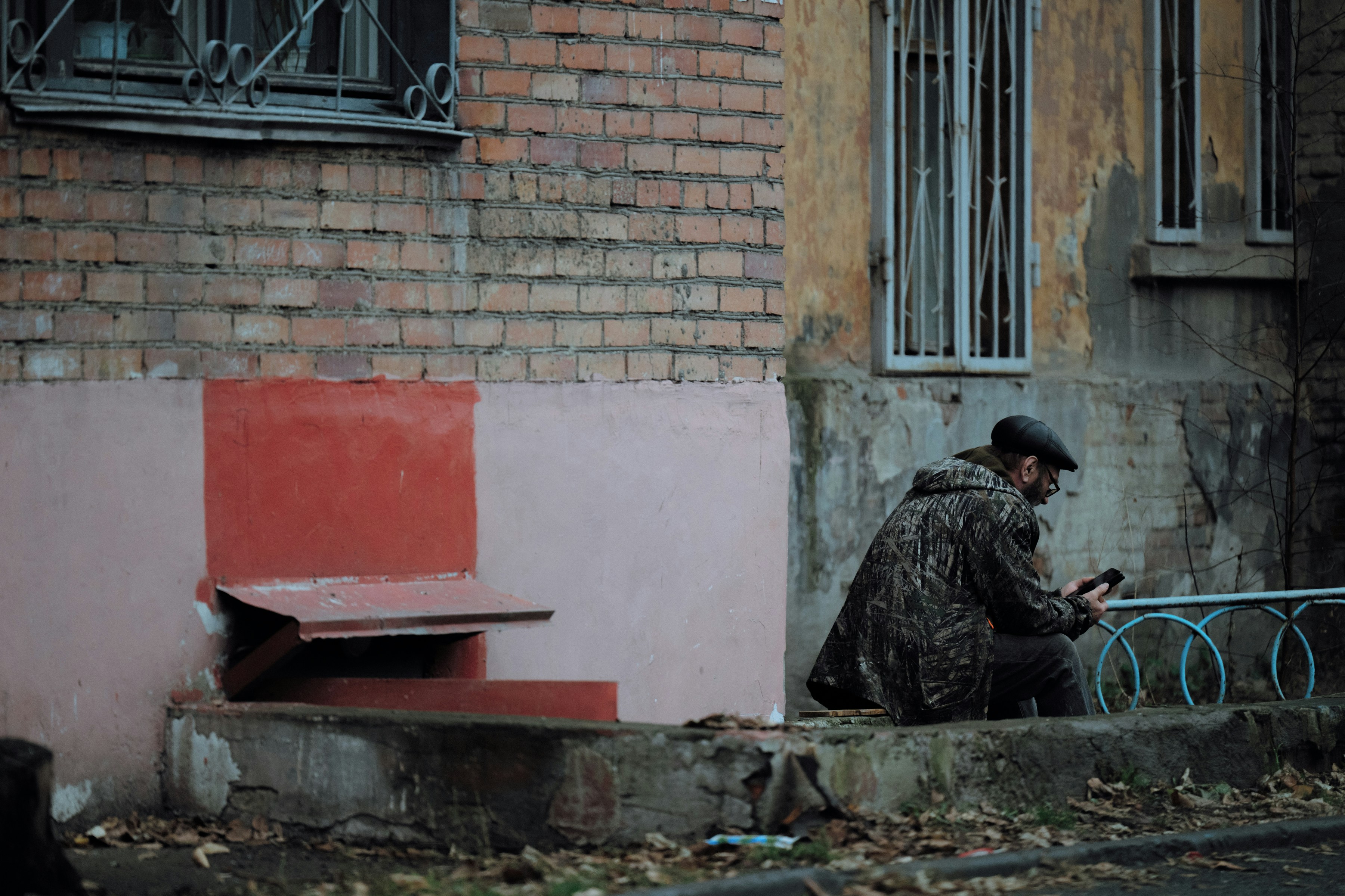 Man in camouflage jacket sitting outside building