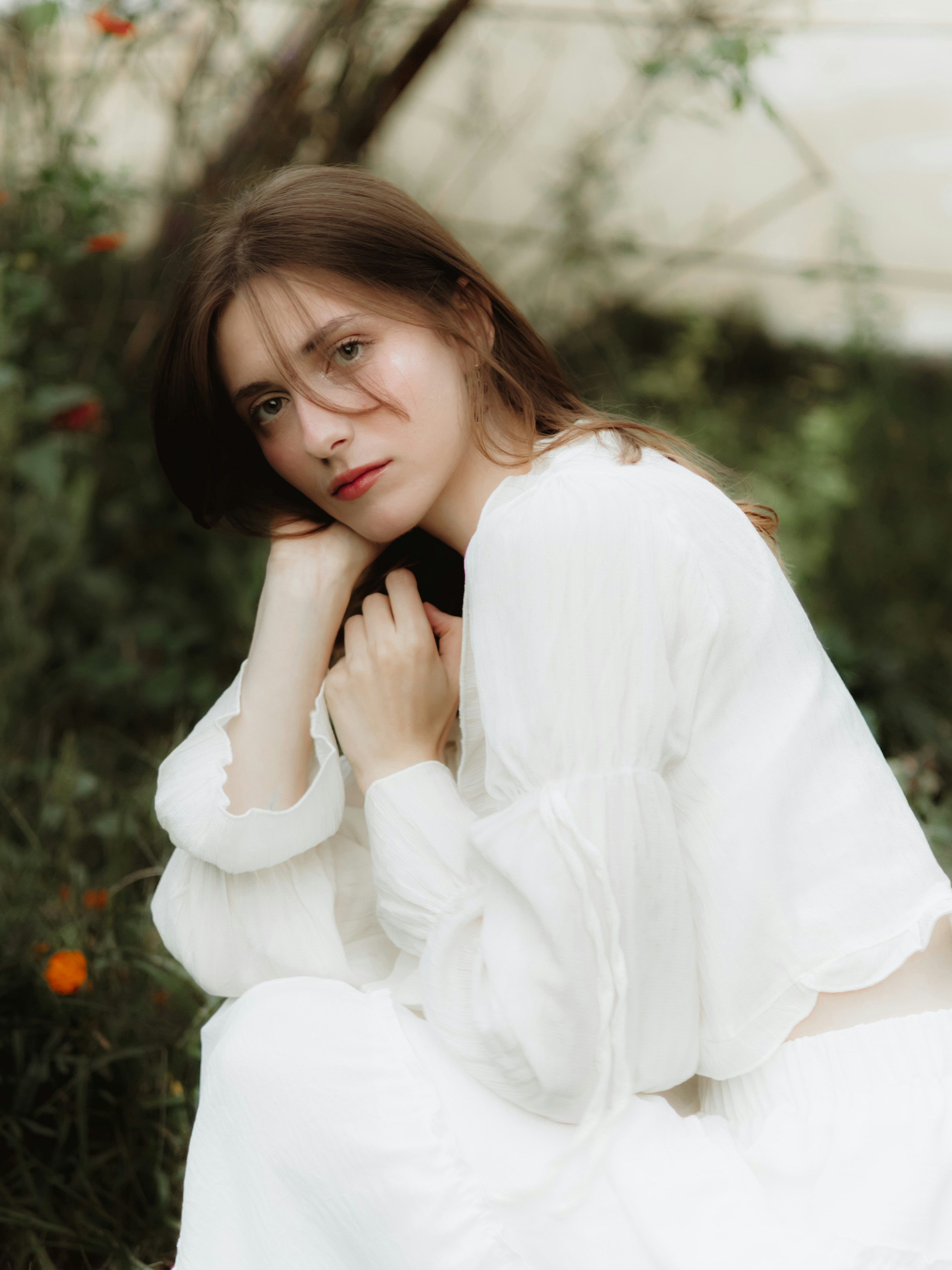 Young woman in white dress with hands near face.
