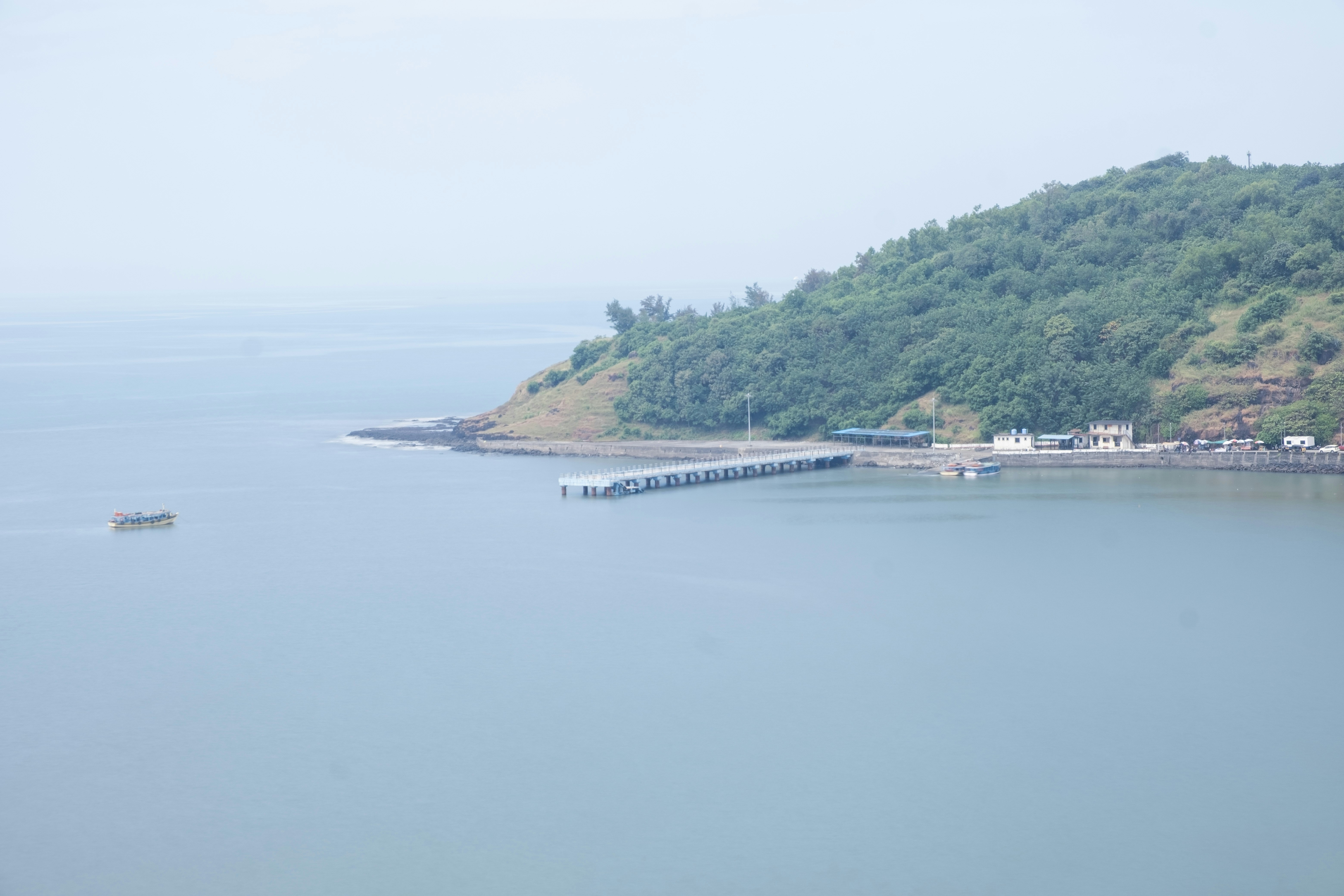 Calm sea meets a green, hilly coastline with a pier.
