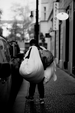 Person carrying large bags down a cobblestone street.