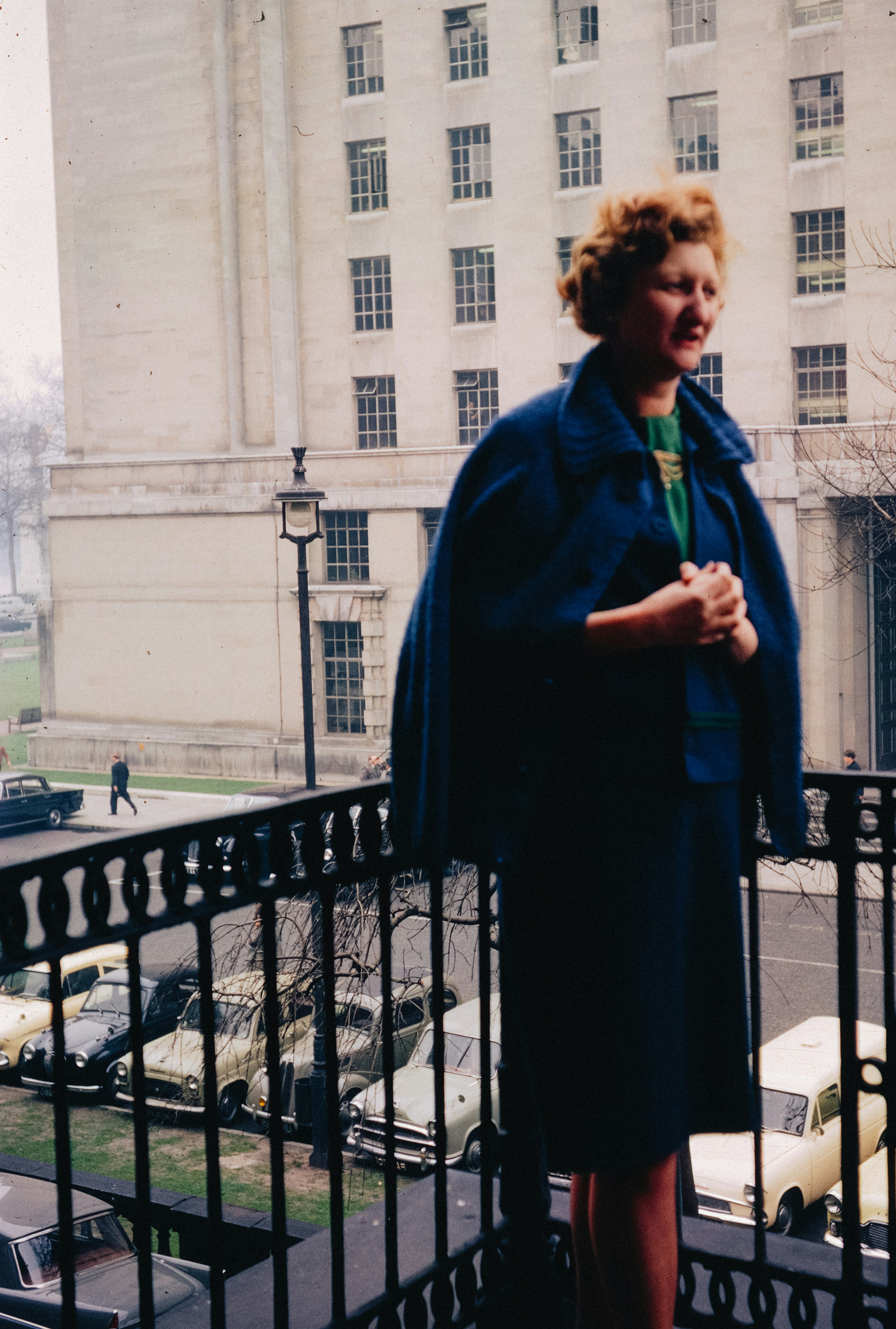 Mulher em pé em uma varanda com vista para a rua.