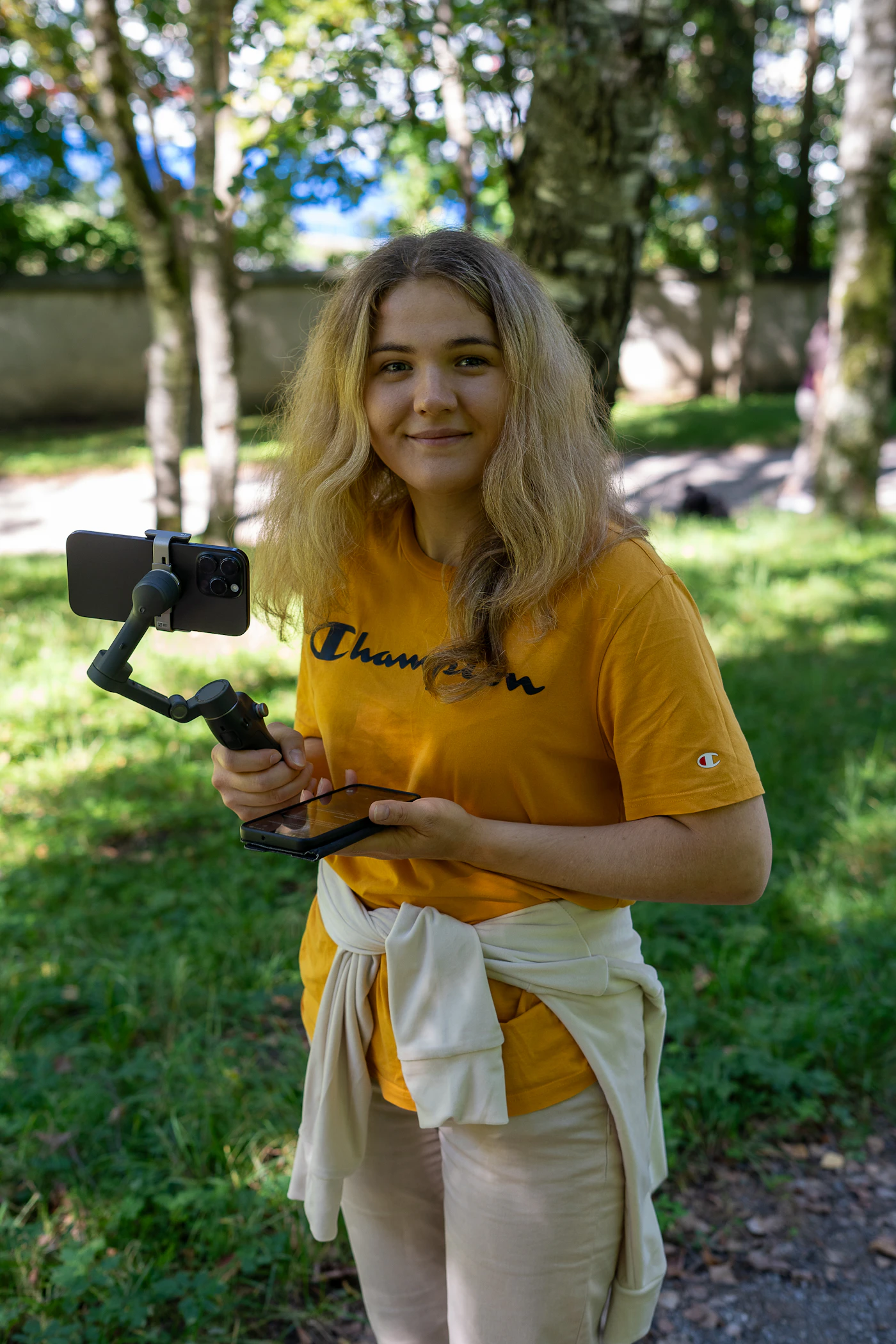 Young woman filming herself with a smartphone on a gimbal outdoors to create varied Instagram Reels ad creative