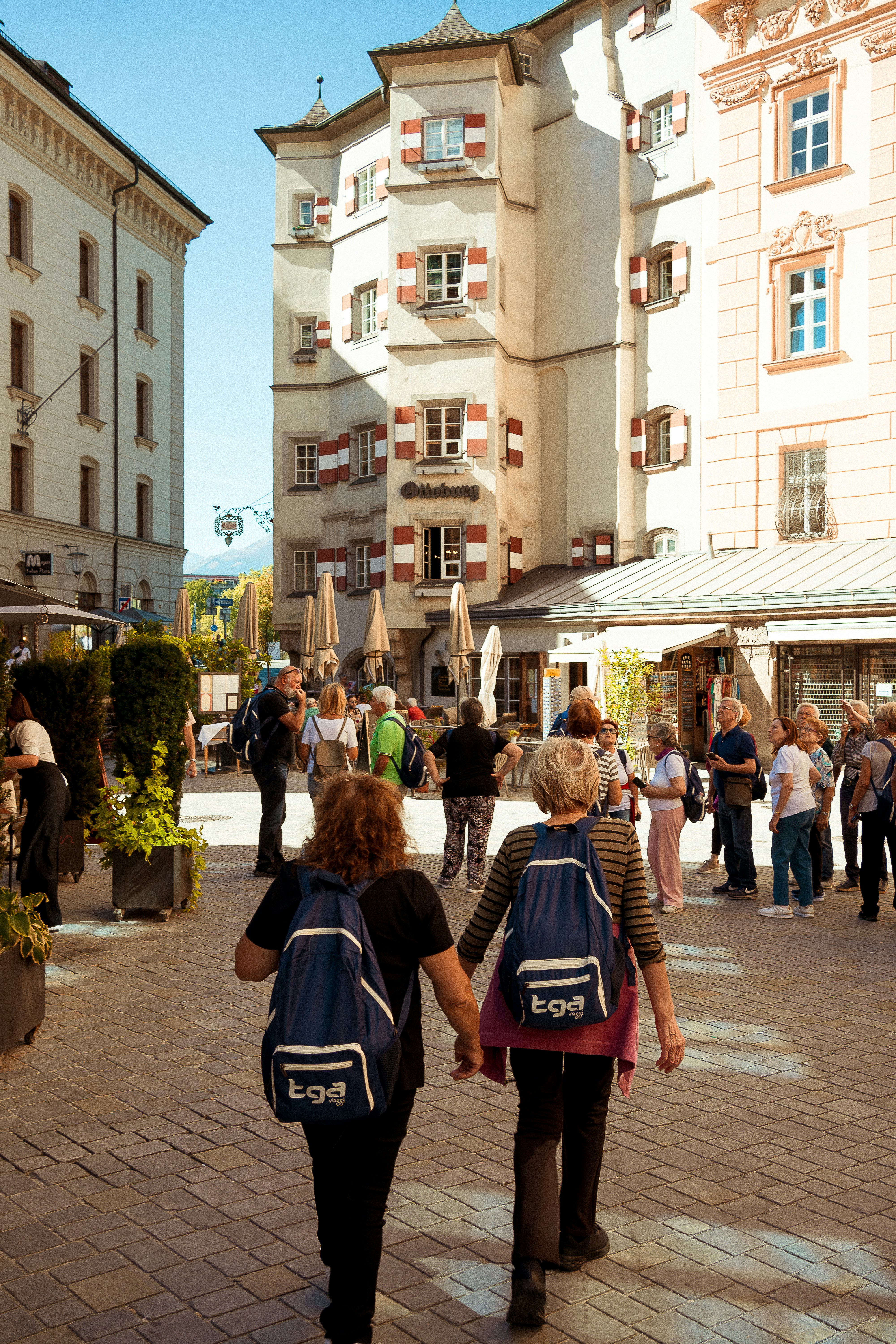 Two women with backpacks walk down a cobblestone street.
