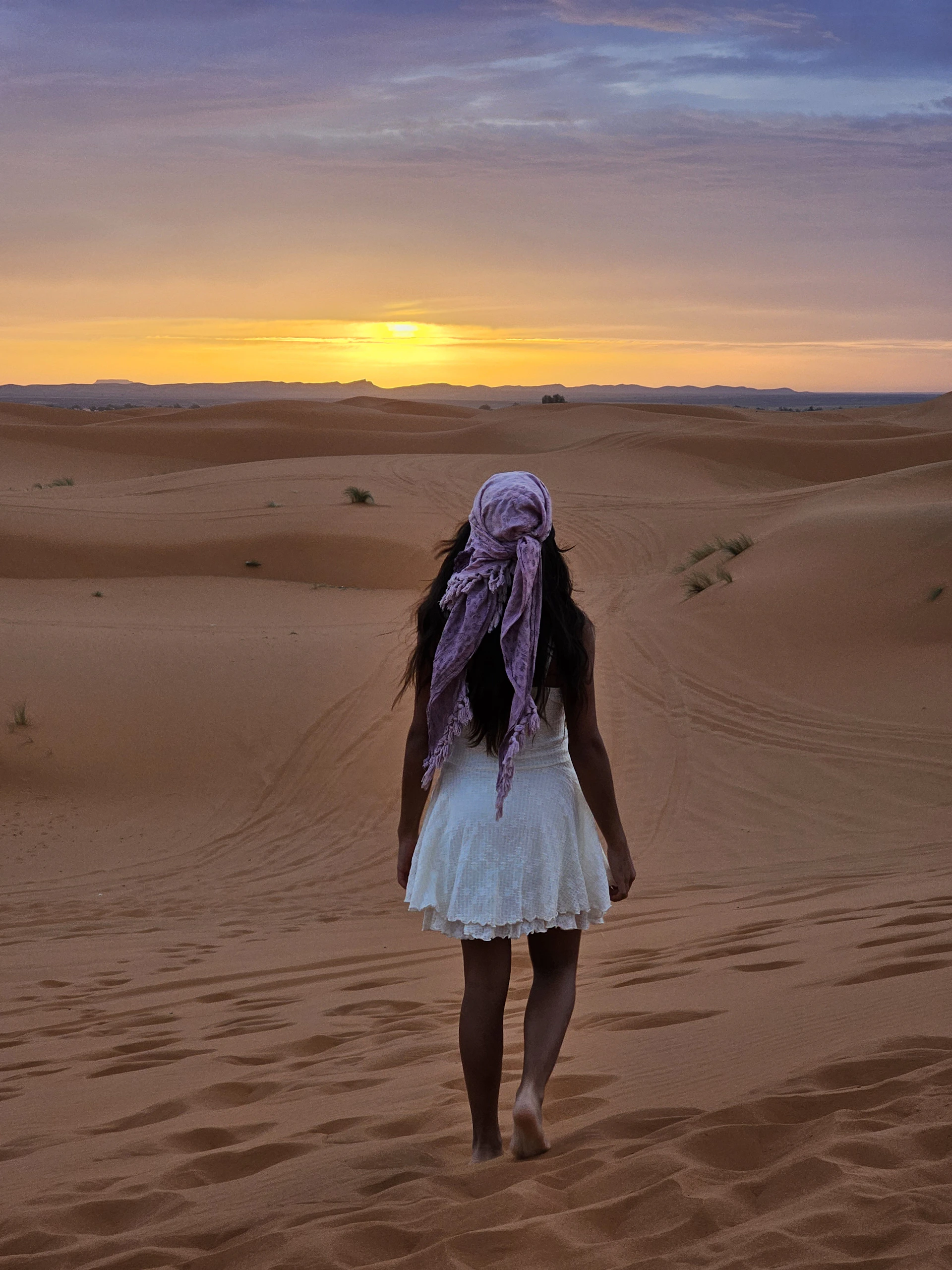Woman walking through desert dunes at sunset