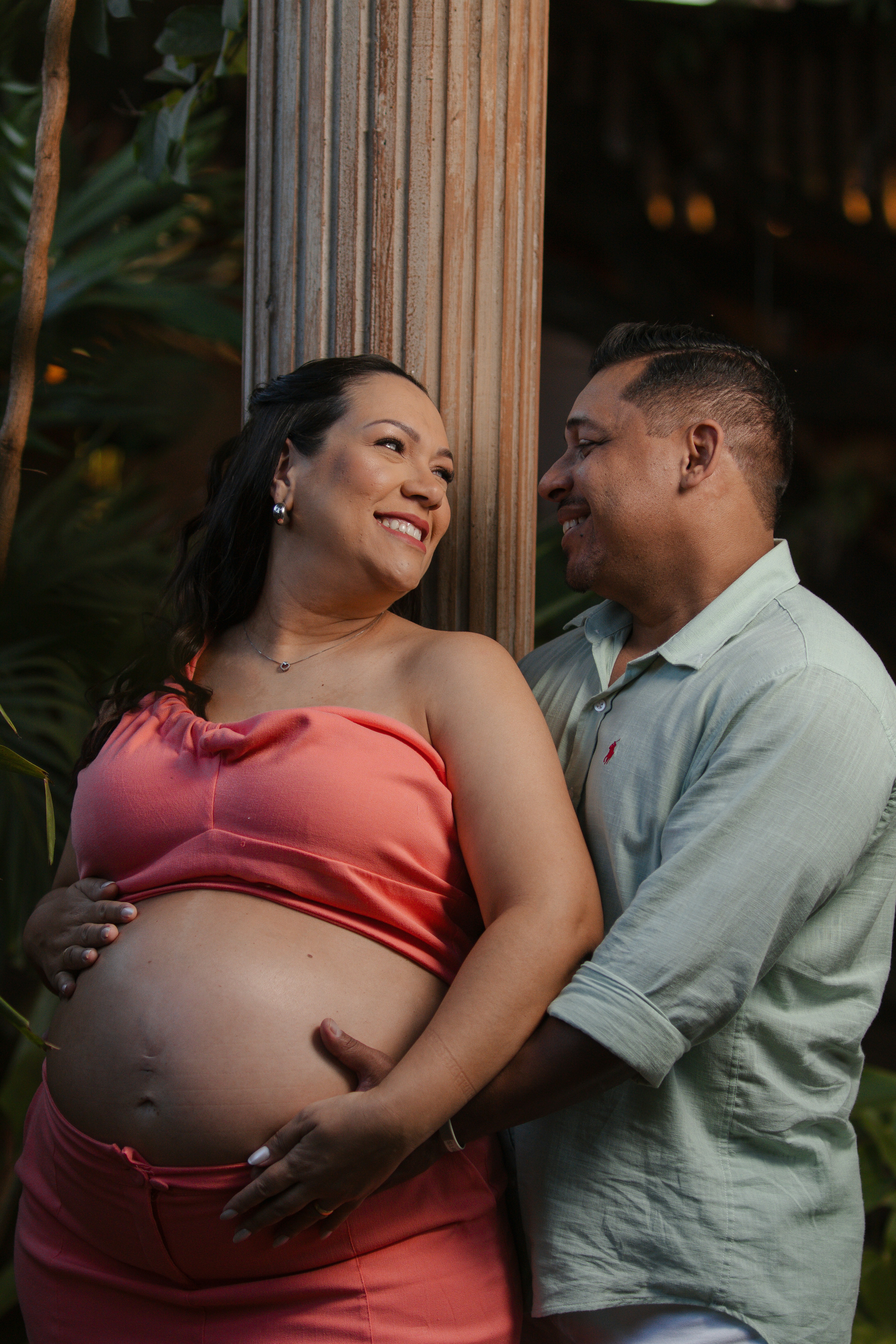 Pregnant couple embracing outdoors near a pillar