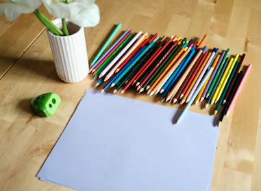 Colored pencils, paper, and vase on wooden table.