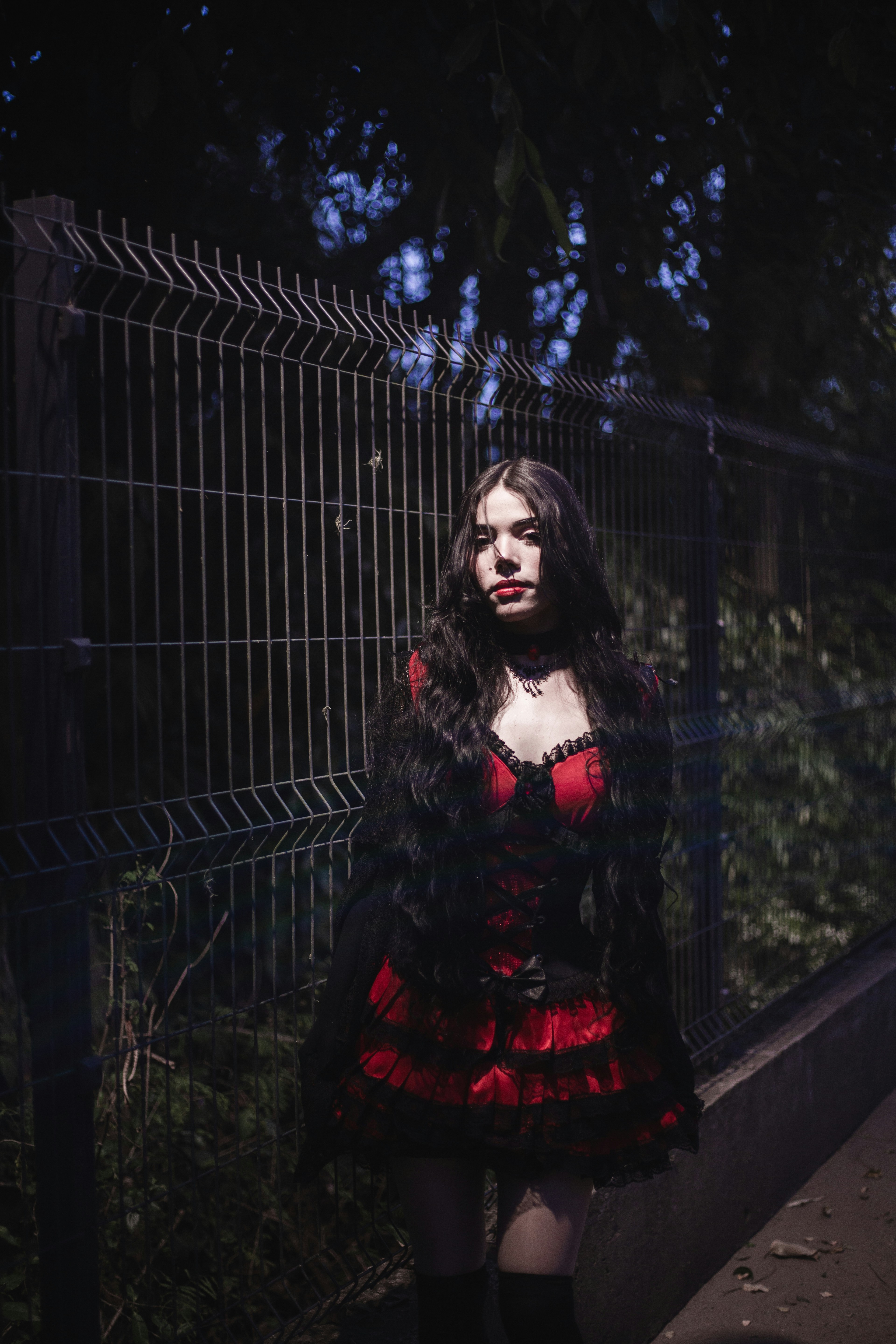 Young woman in red and black dress near fence.