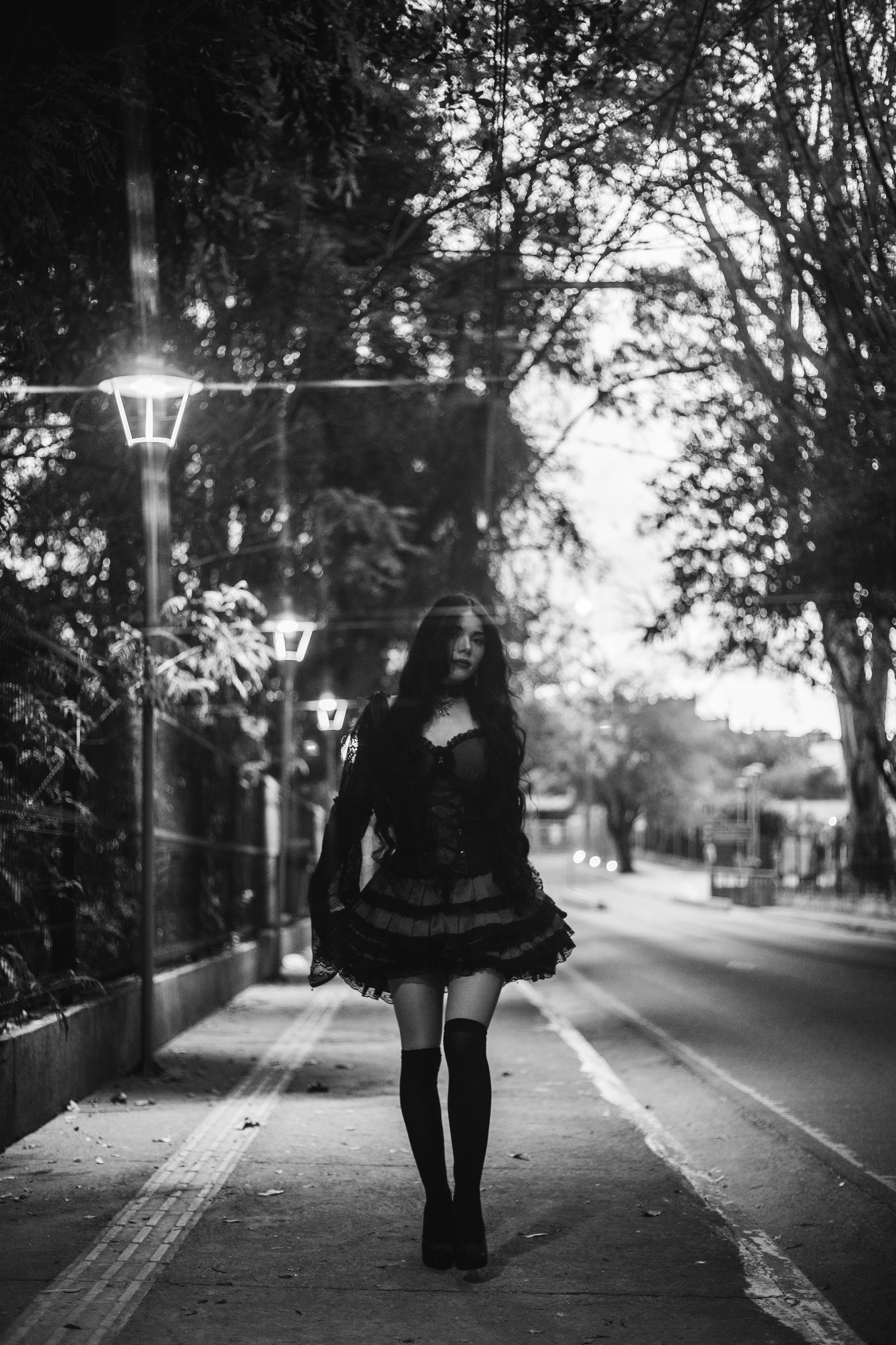 A woman walks down a tree-lined street at night.