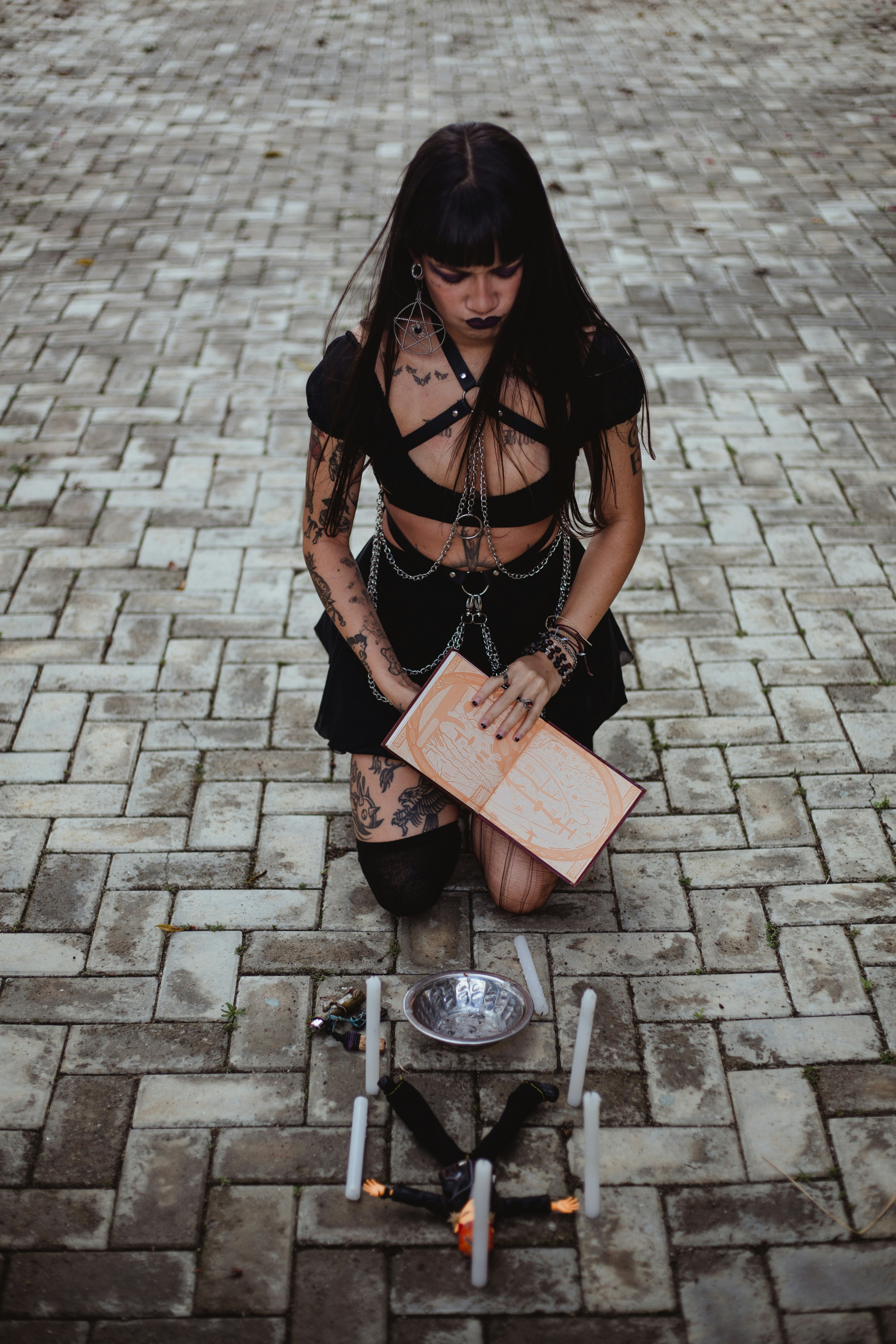 Wanita berpakaian gothic berlutut dengan buku dan lilin.