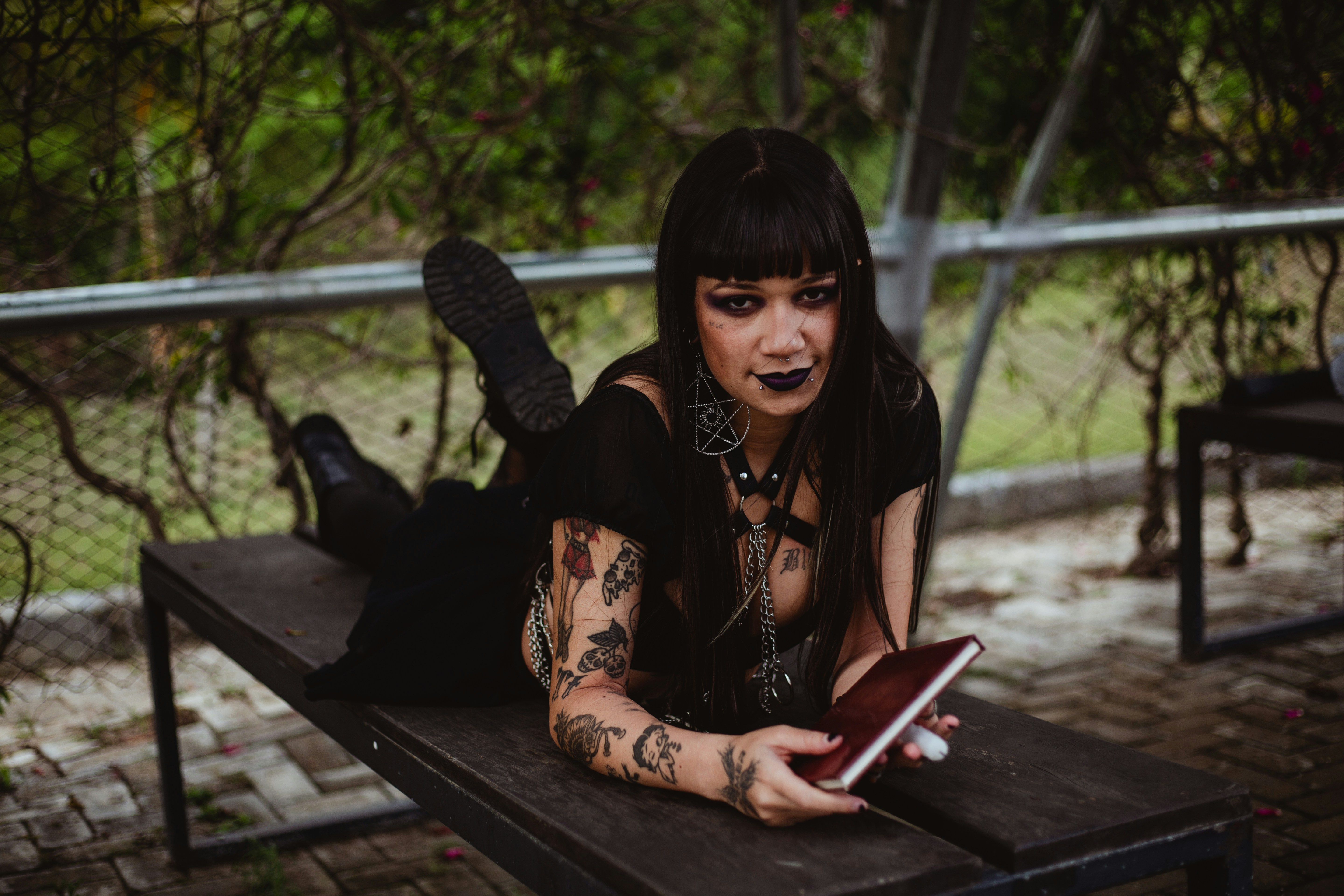 Mulher com composição escura e tatuagens que encontram-se no banco