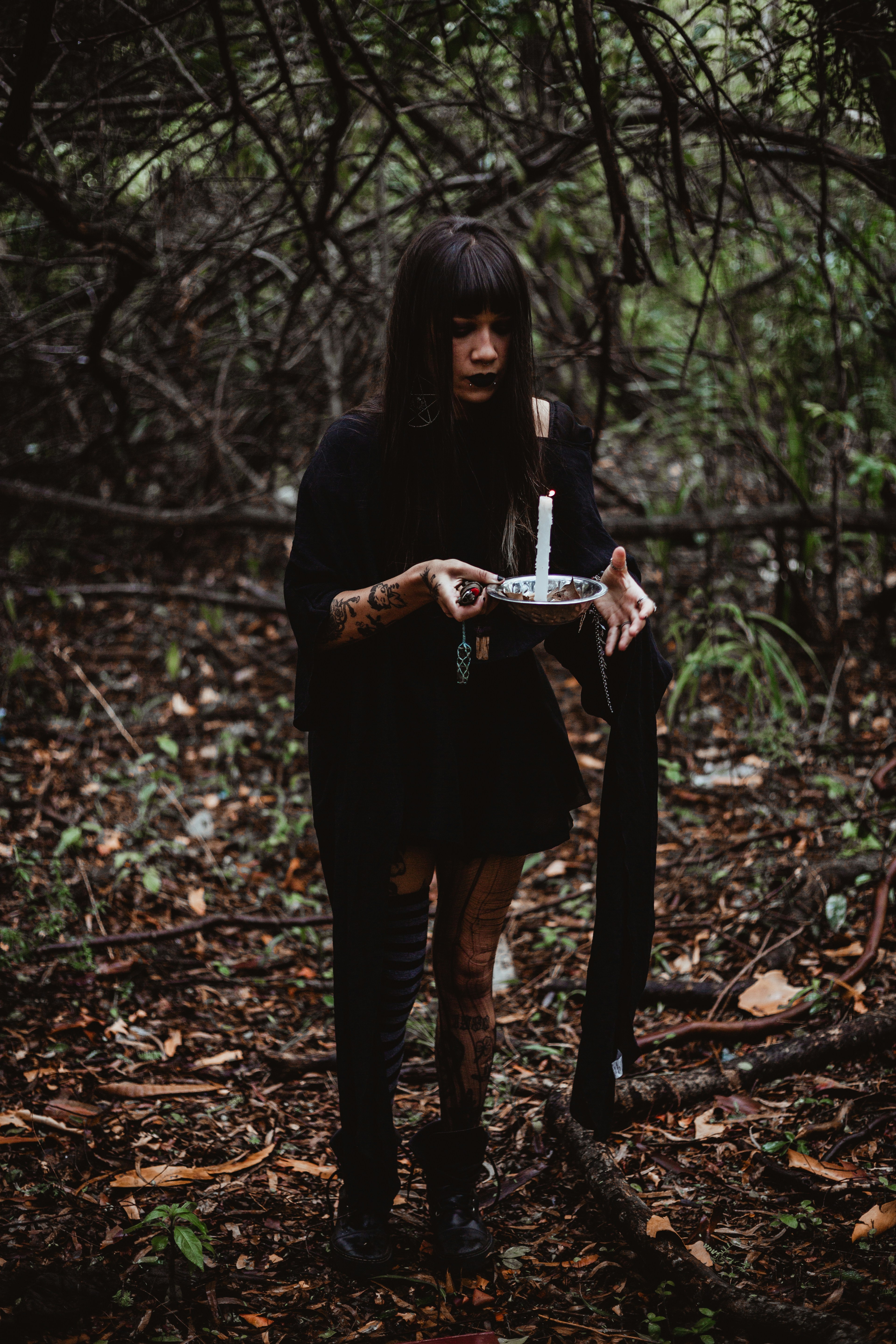 Woman holding a lit candle in a dark forest.