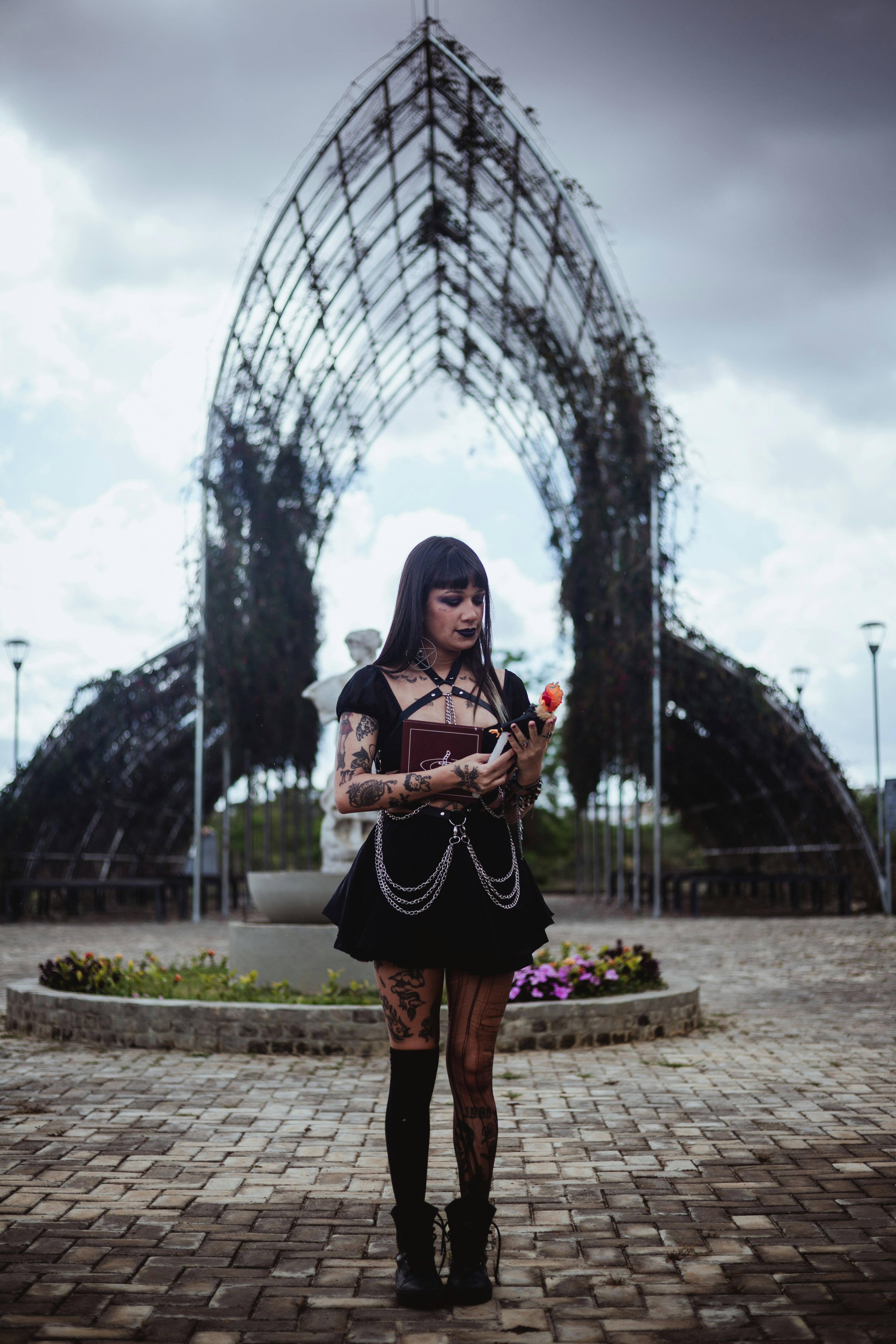 Wanita berpakaian gothic memegang mawar di dekat gapura.