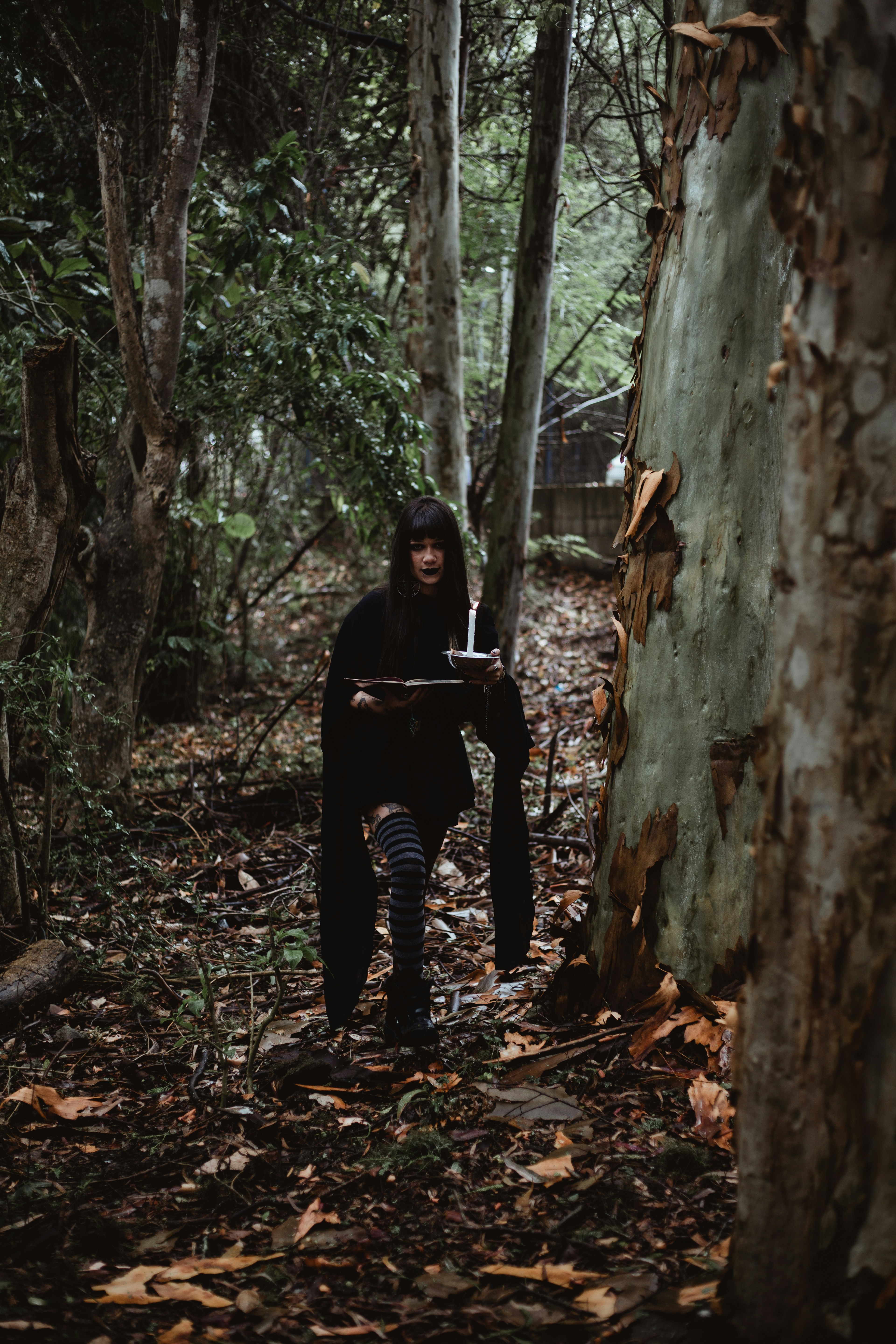 Woman holding a candle and book in a dark forest.