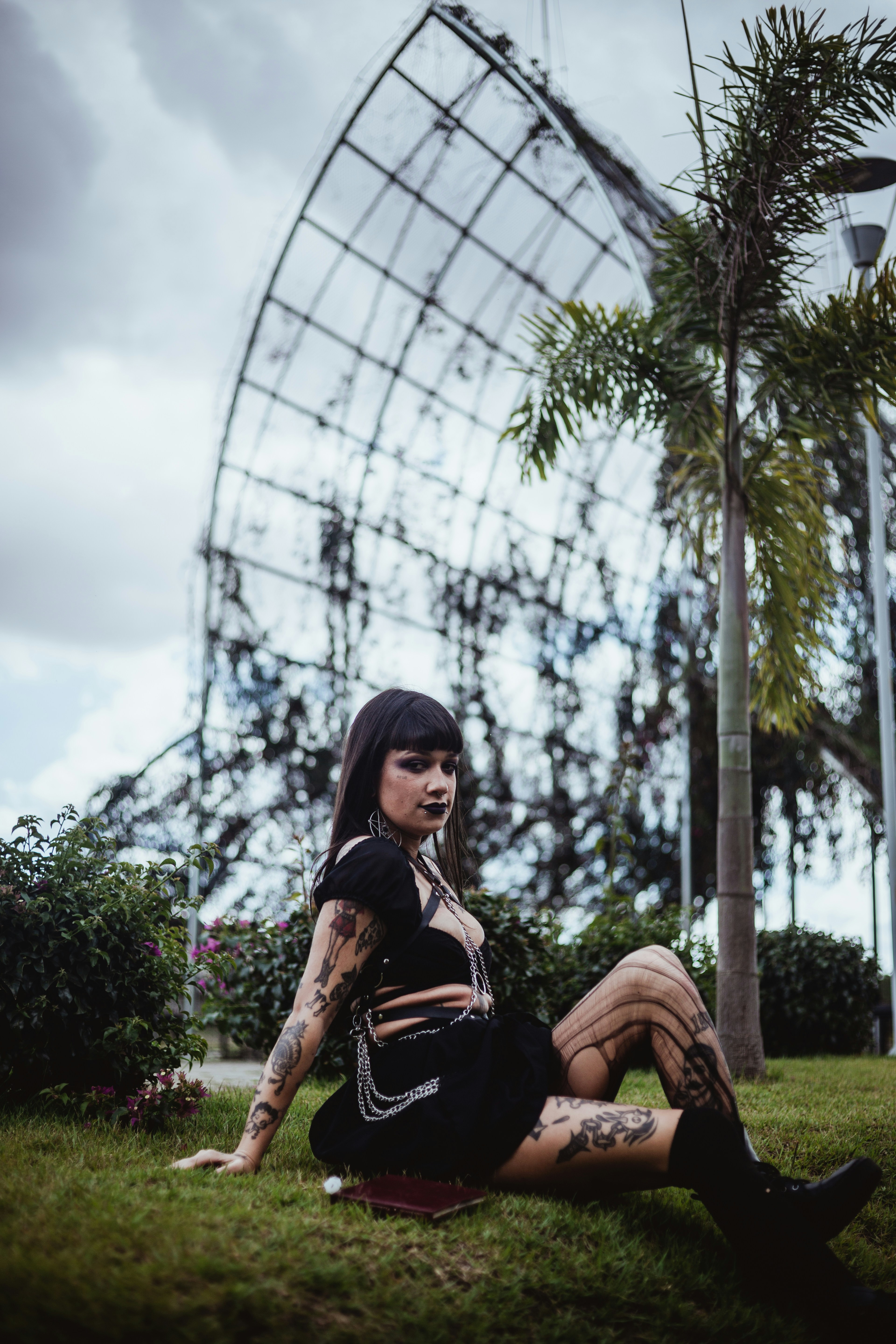 Woman with tattoos sits on grass near geodesic dome.