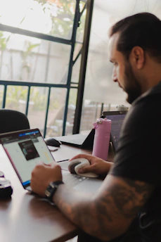 Man working on laptop with pink water bottle nearby