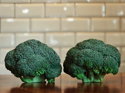 Two heads of fresh broccoli on a wooden table.