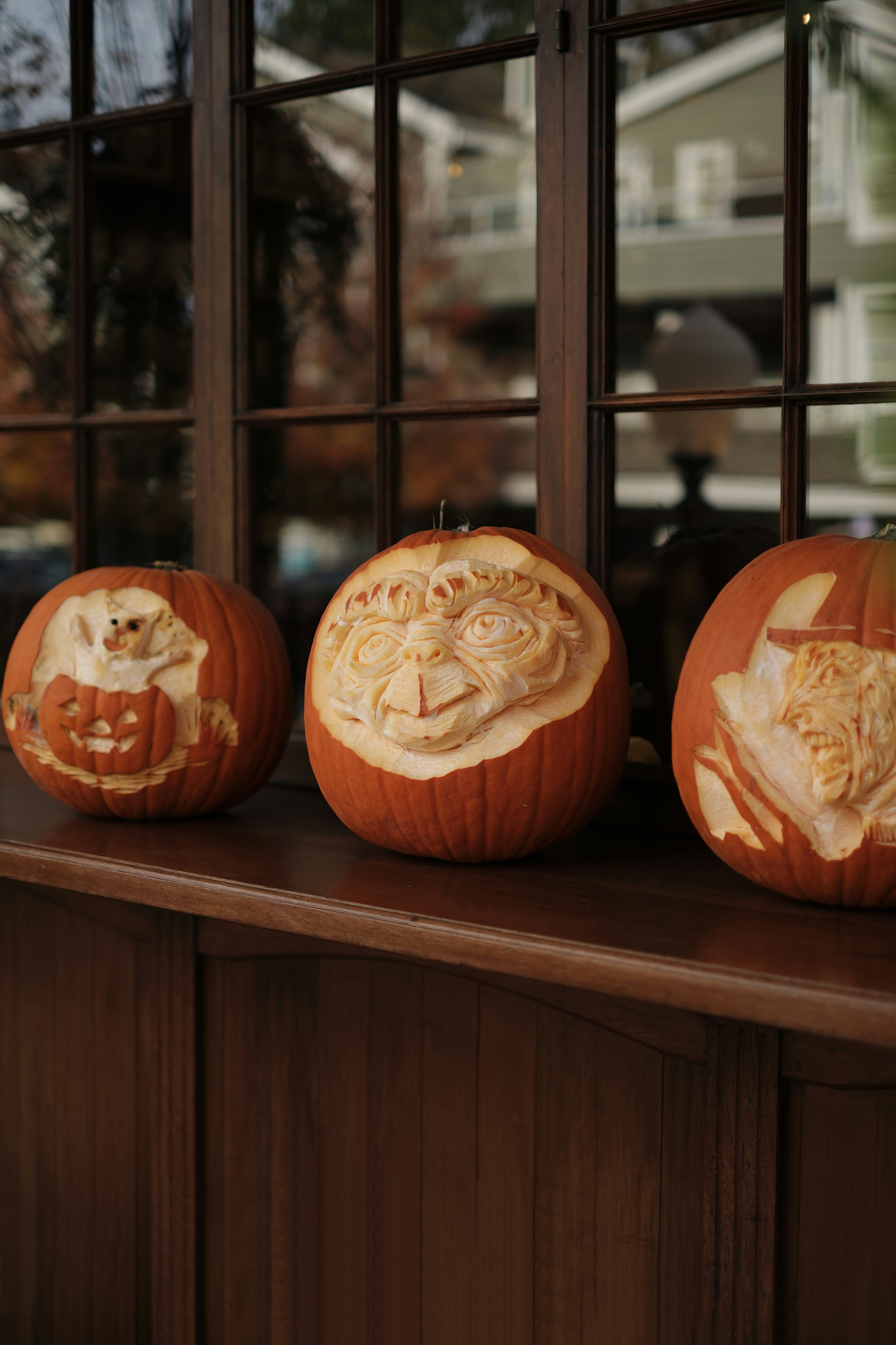 Three carved pumpkins sit on a windowsill.