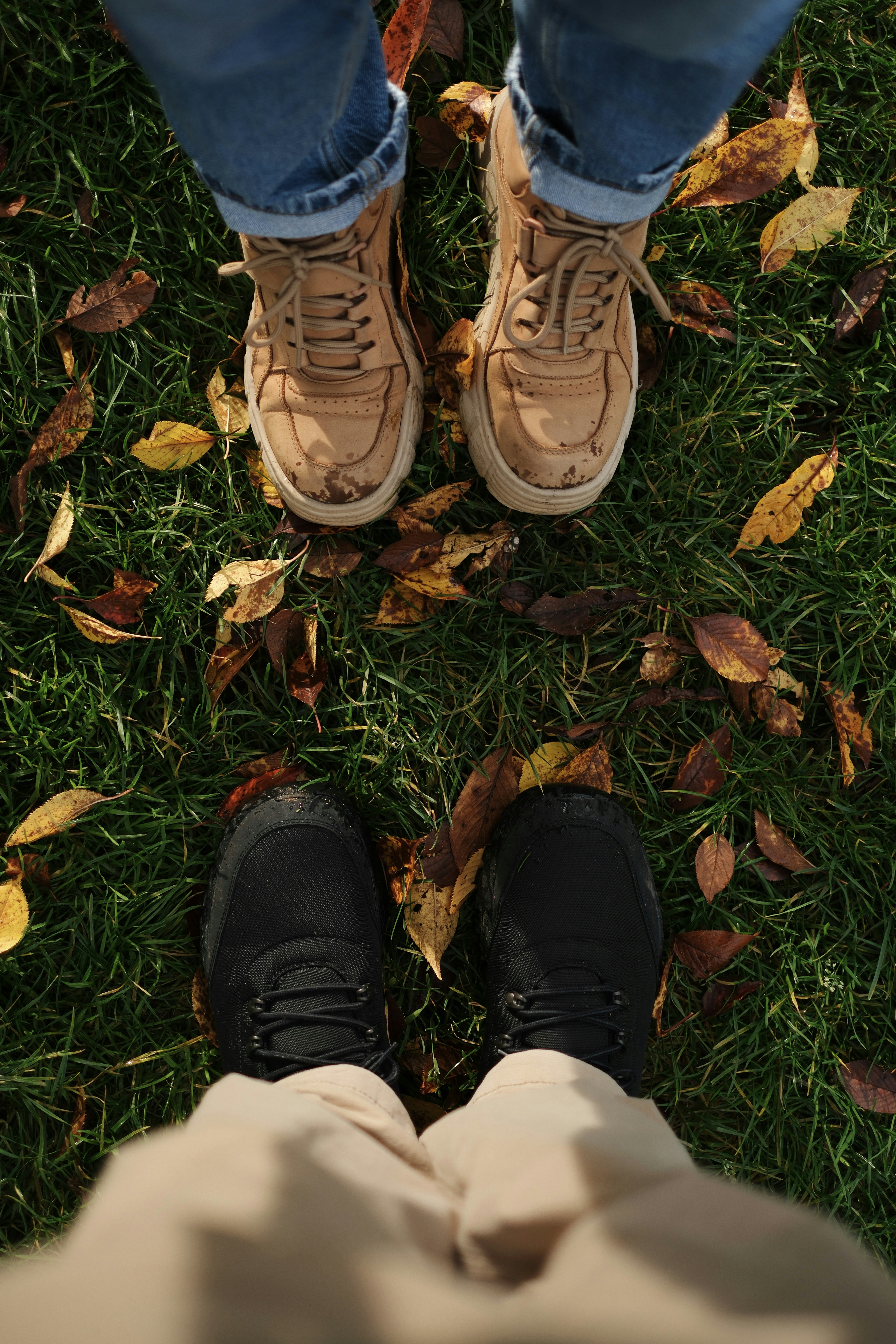 Two pairs of feet standing on grass with fallen leaves.