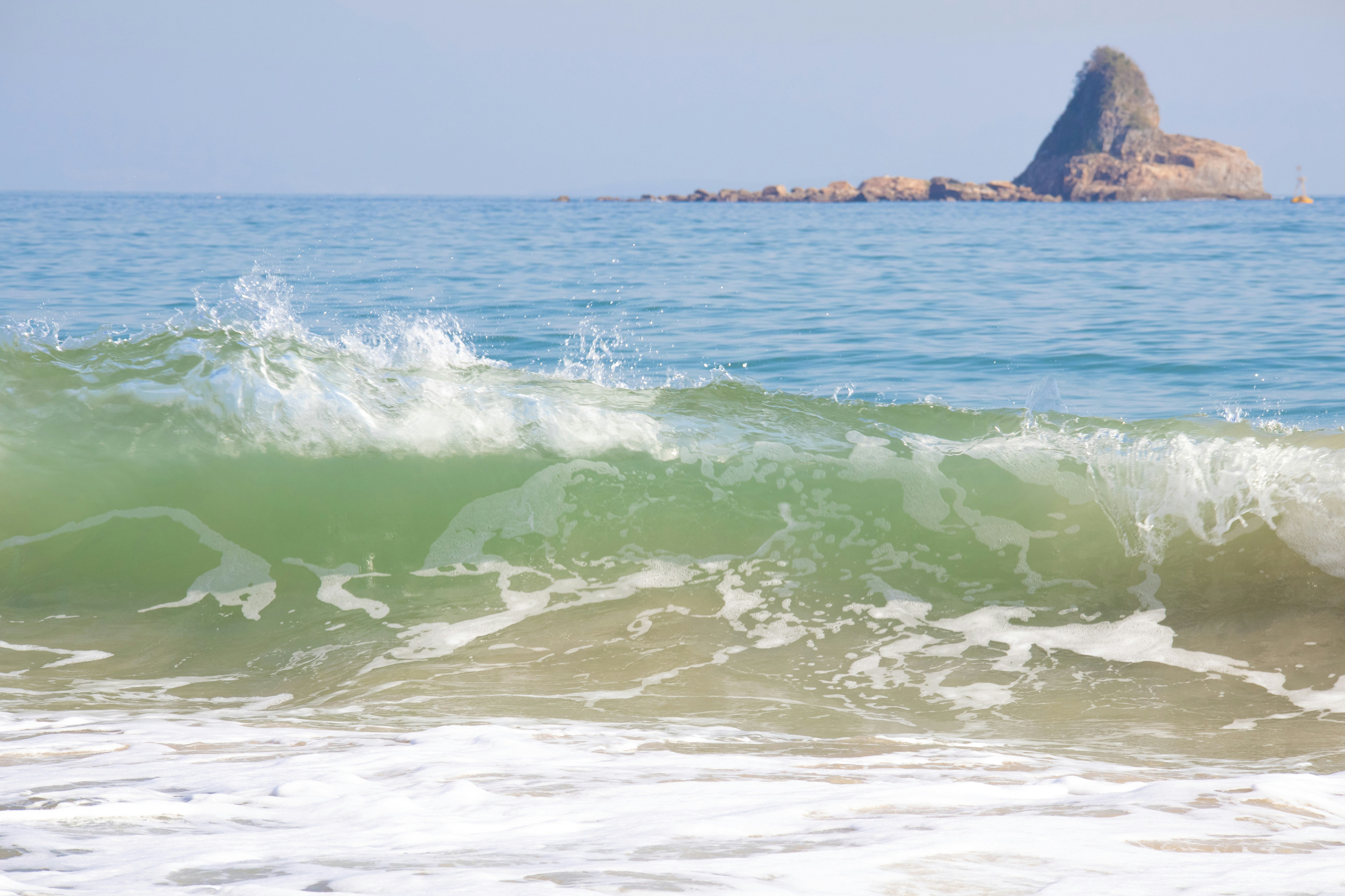 A green wave crashes on a sandy beach.