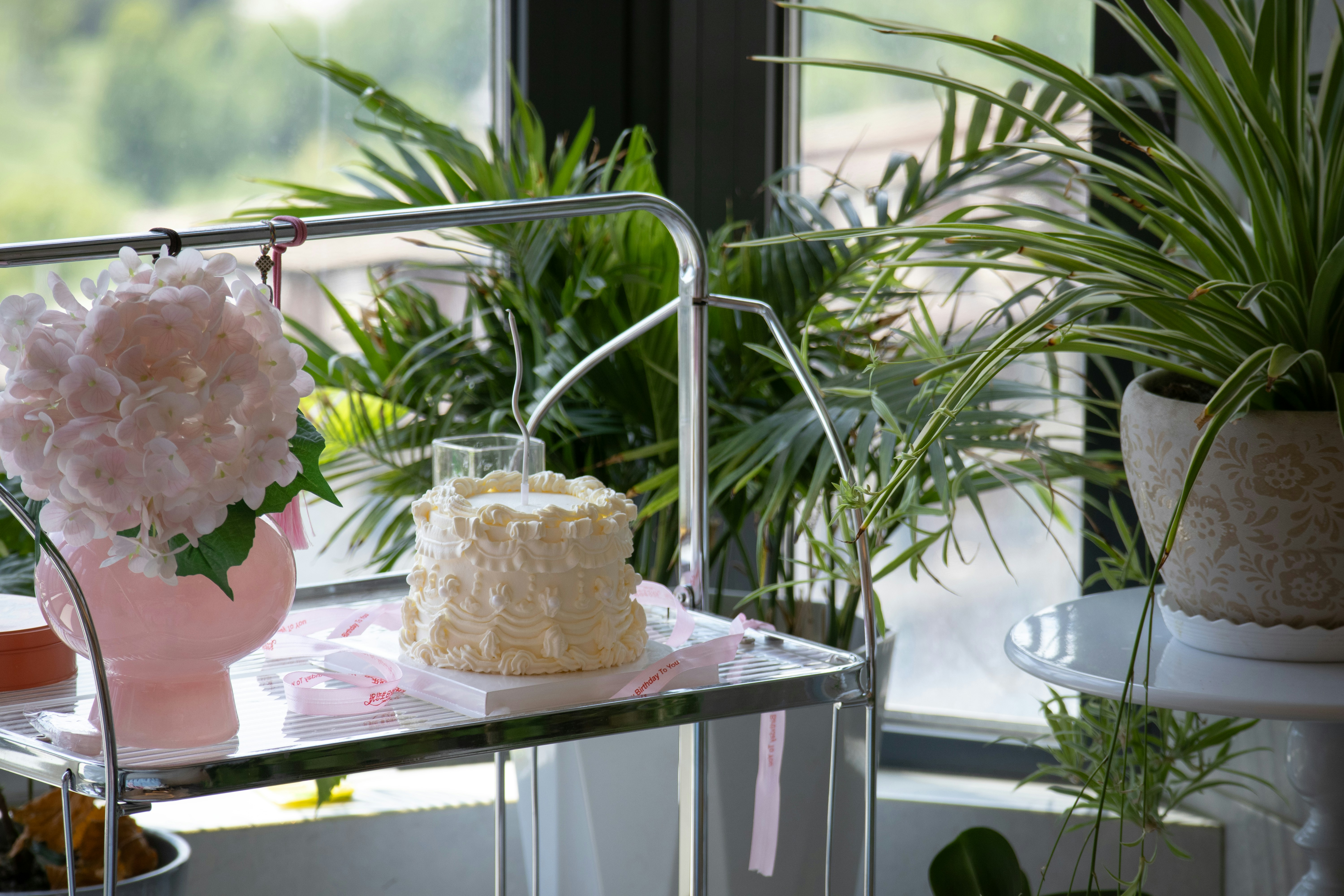 Small white cake with pink flowers and plants.