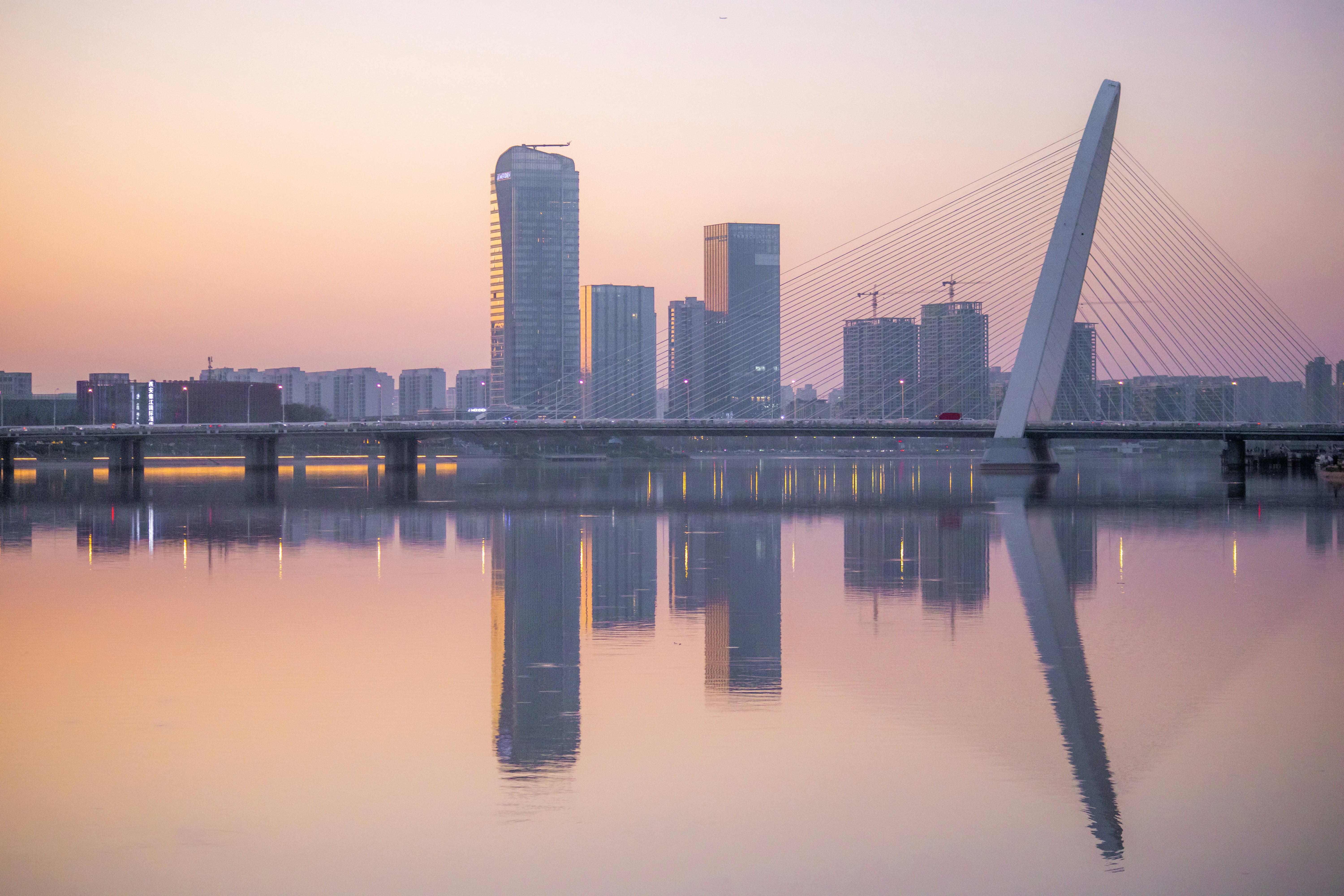 City skyline with bridge reflected in water at sunset