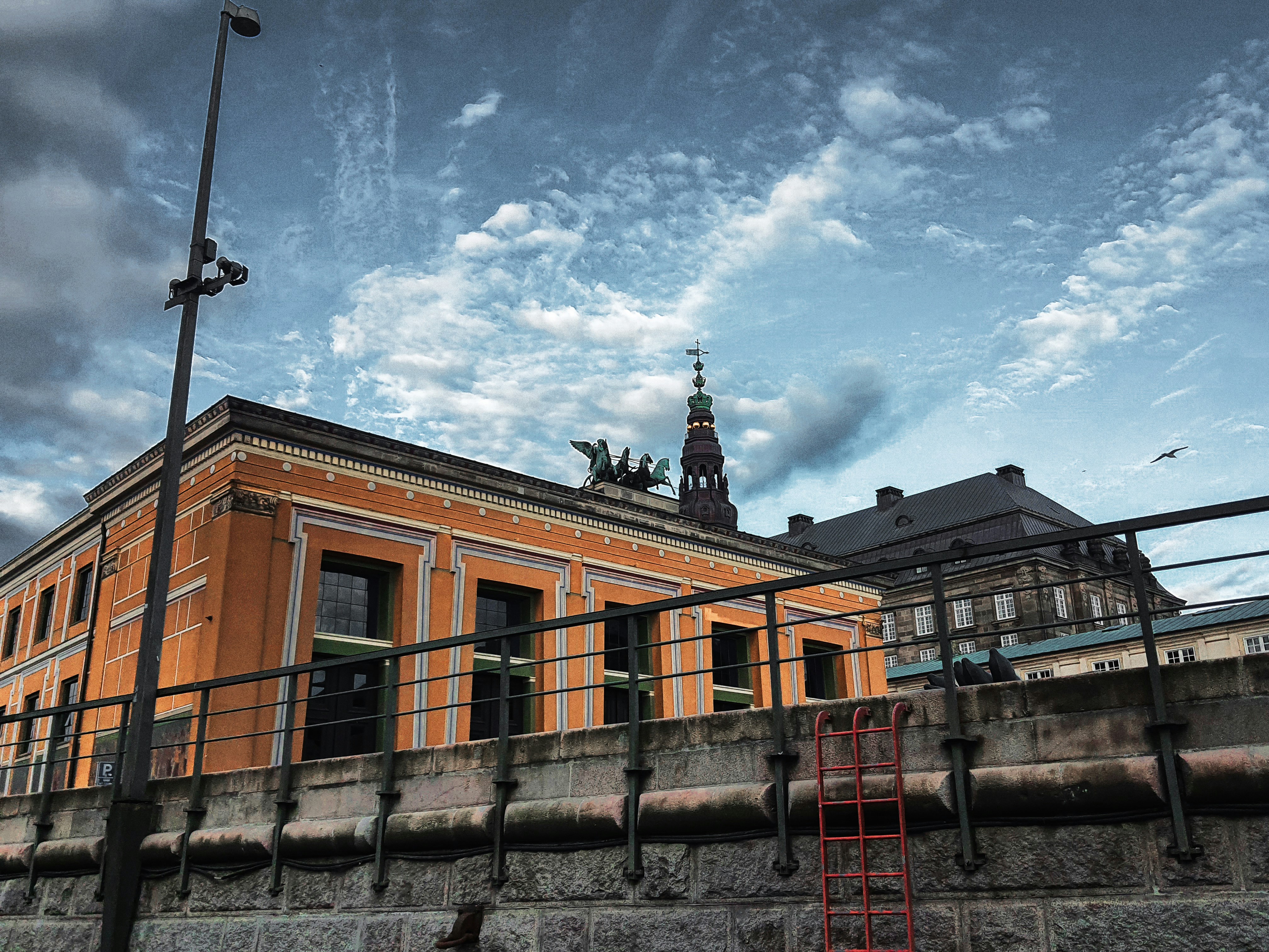 Orange building with a tower against cloudy sky.