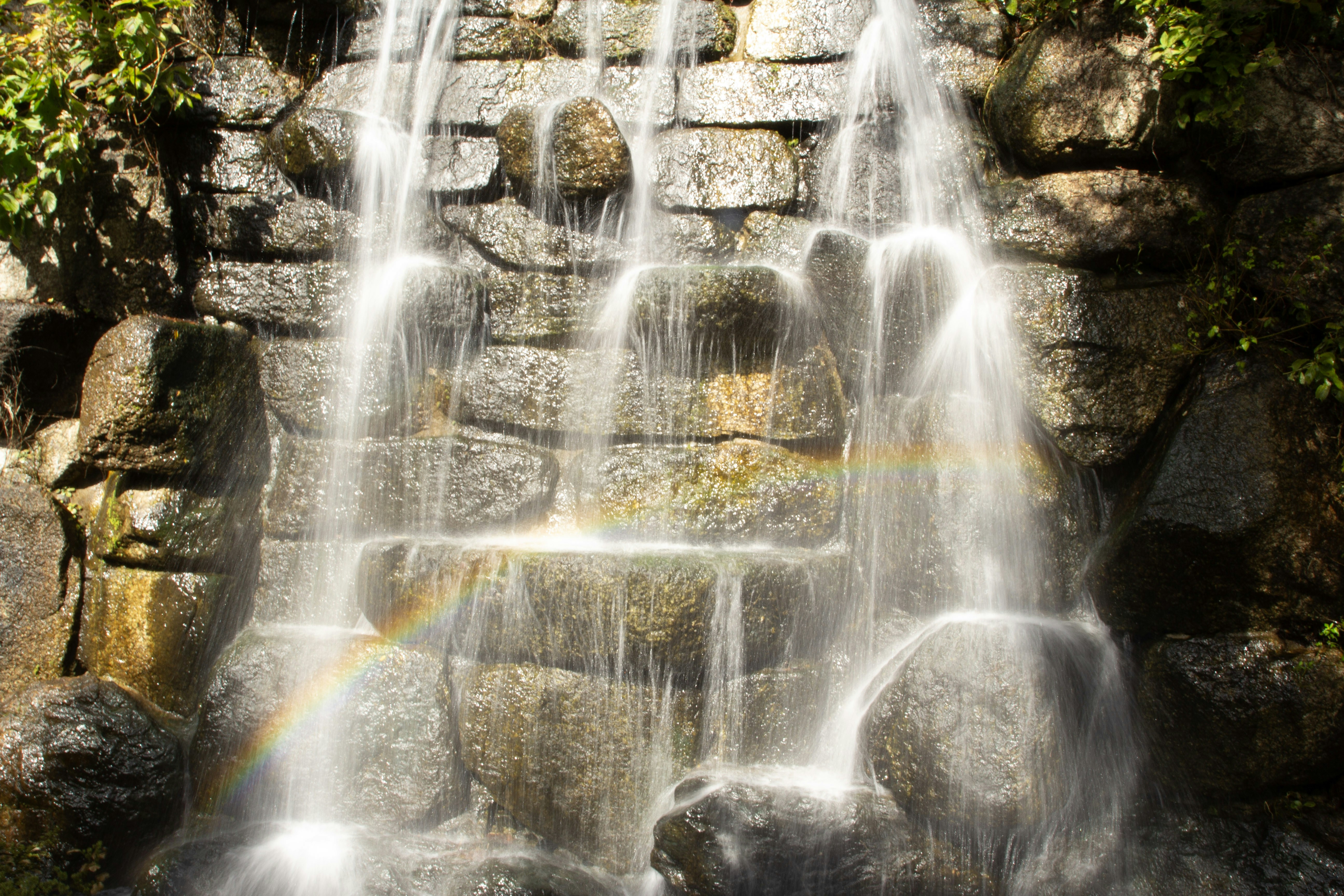 A waterfall cascades down a rocky wall creating a rainbow.